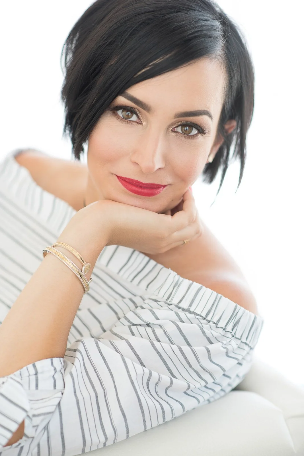 Woman with short dark hair and off shoulder shirt with white background looks into camera for her personal branding shoot.