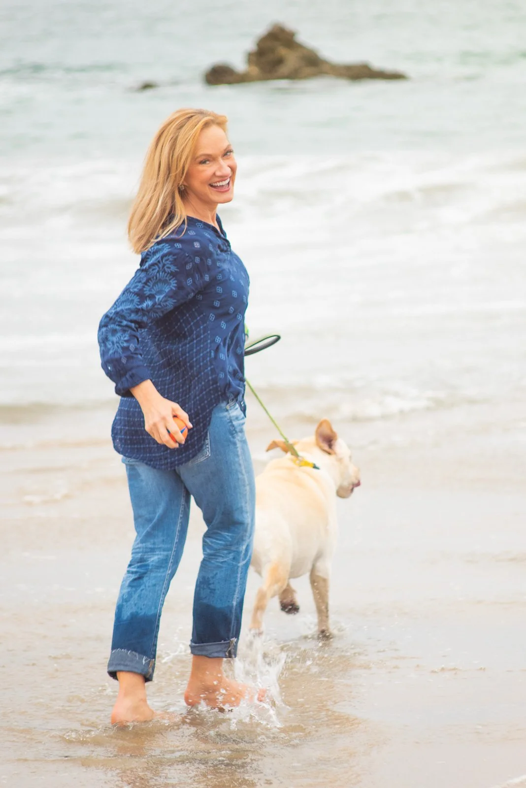 Professional woman walking on beach with dog during relaxed lifestyle branding photography session.