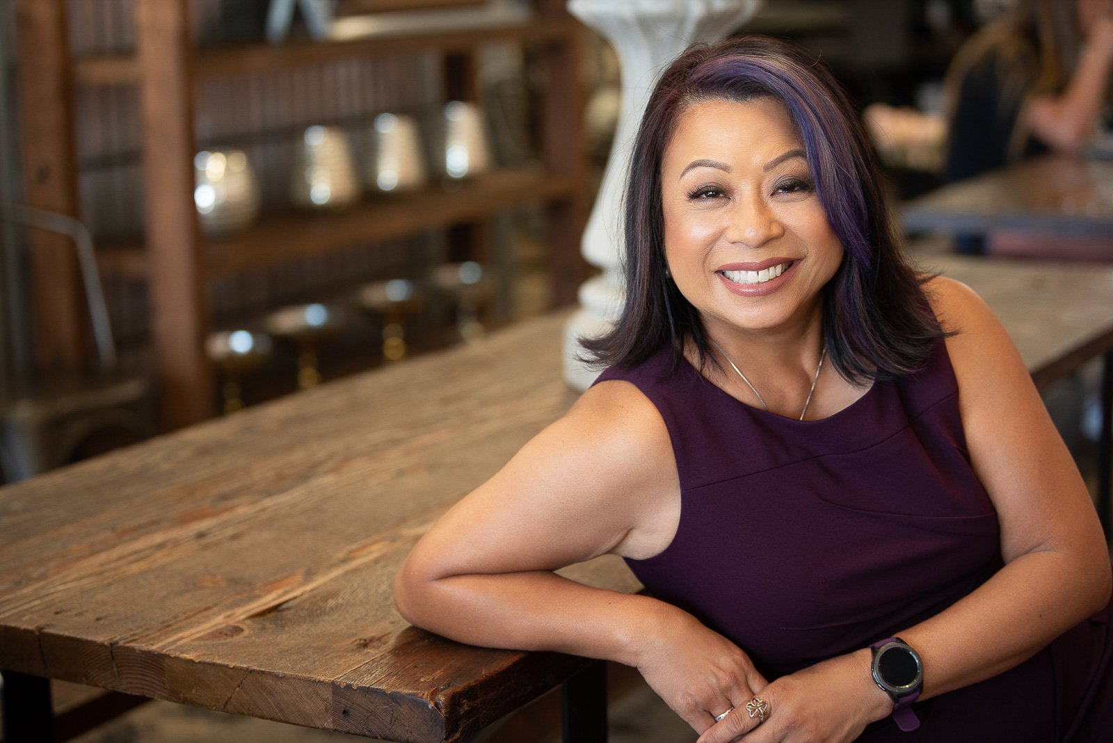 Female service business professional wearing purple leans back against wooden table
