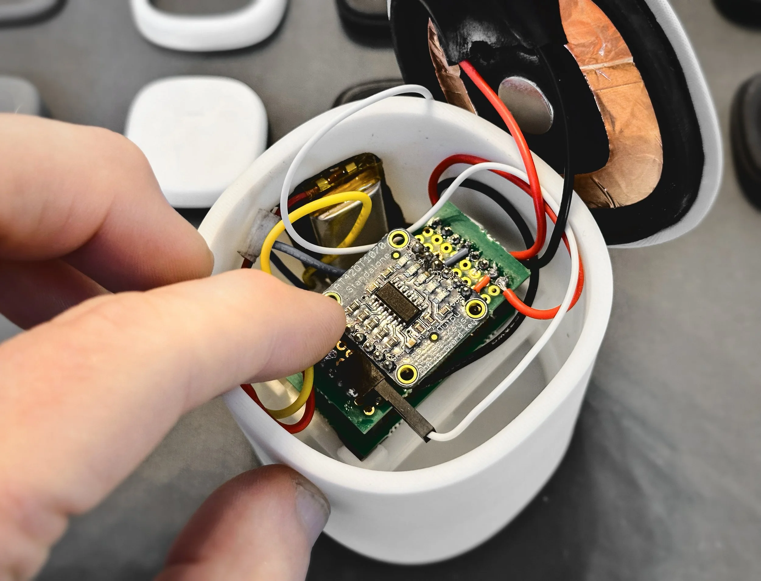 Close-up of an open electronic device with multicolored wires and circuit board inside a white plastic casing.