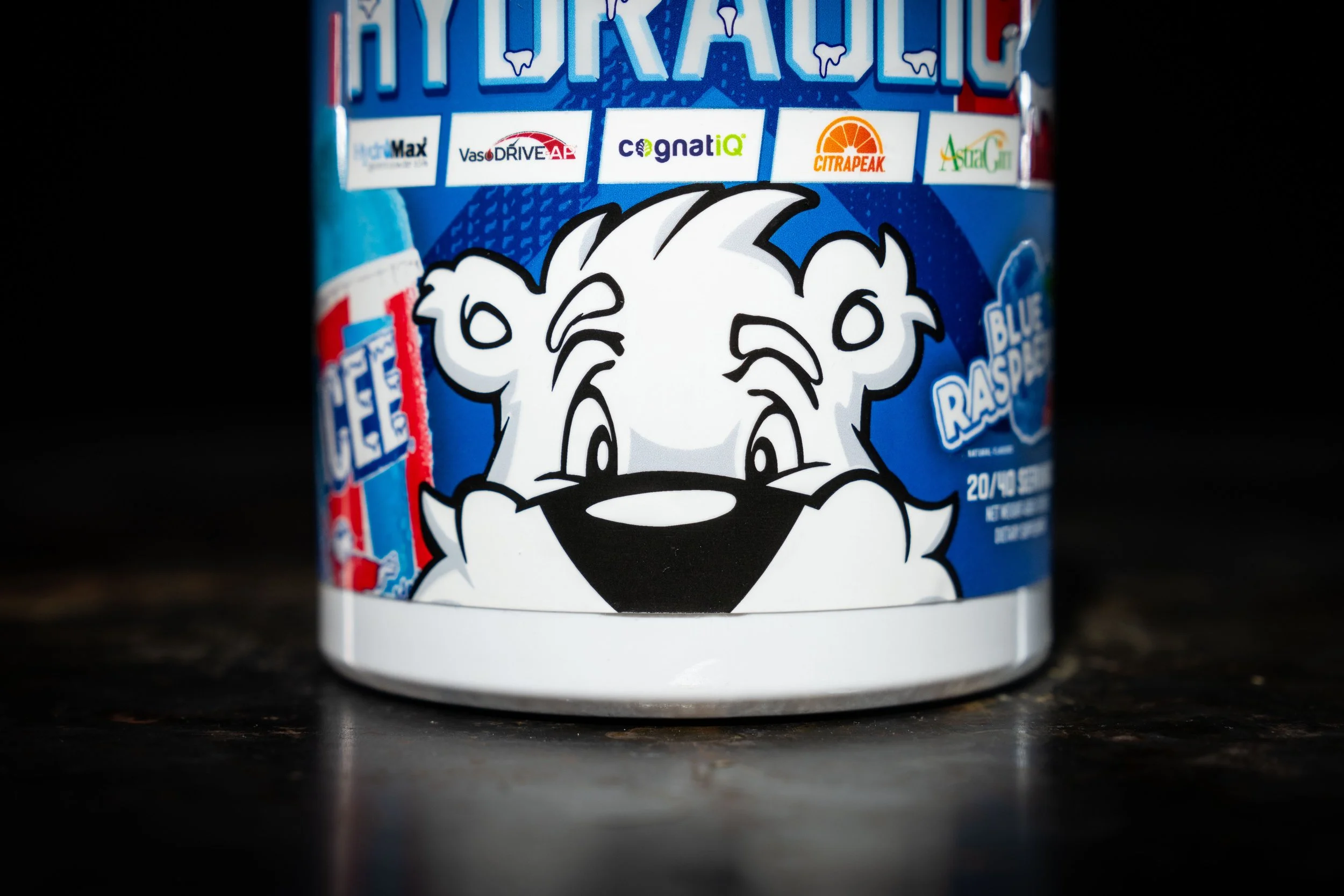 Part of a blue container of ice cream featuring a cartoon white tiger with black and gray facial markings, a playful expression, and a black nose. The container has a label indicating it's blue raspberry flavor.
