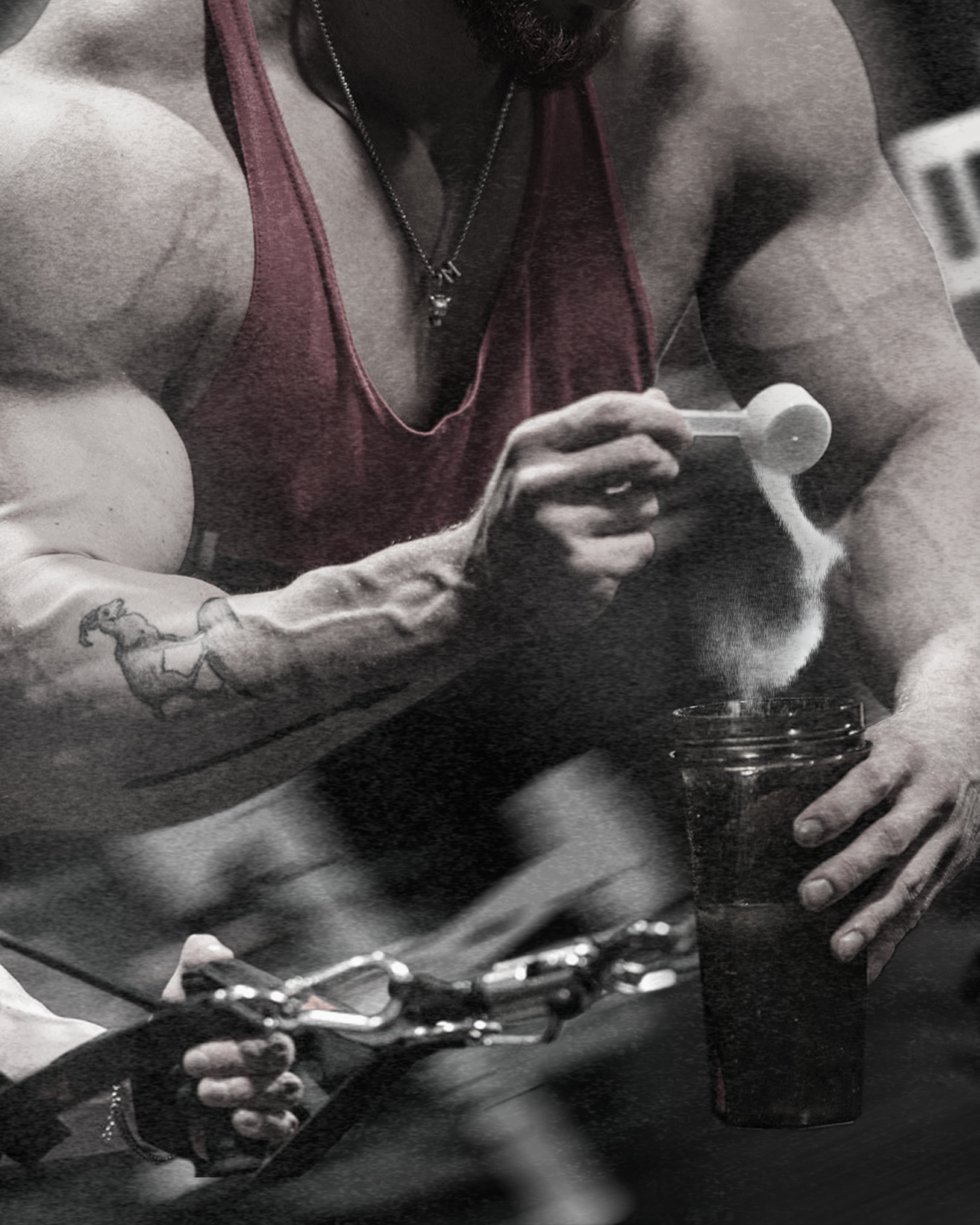 A woman with muscular arms and a tattoo on her forearm is sitting at a table, wearing a sleeveless top and a necklace with a pendant. She is looking at her phone with her fingers on the screen and has a glass of water in front of her.