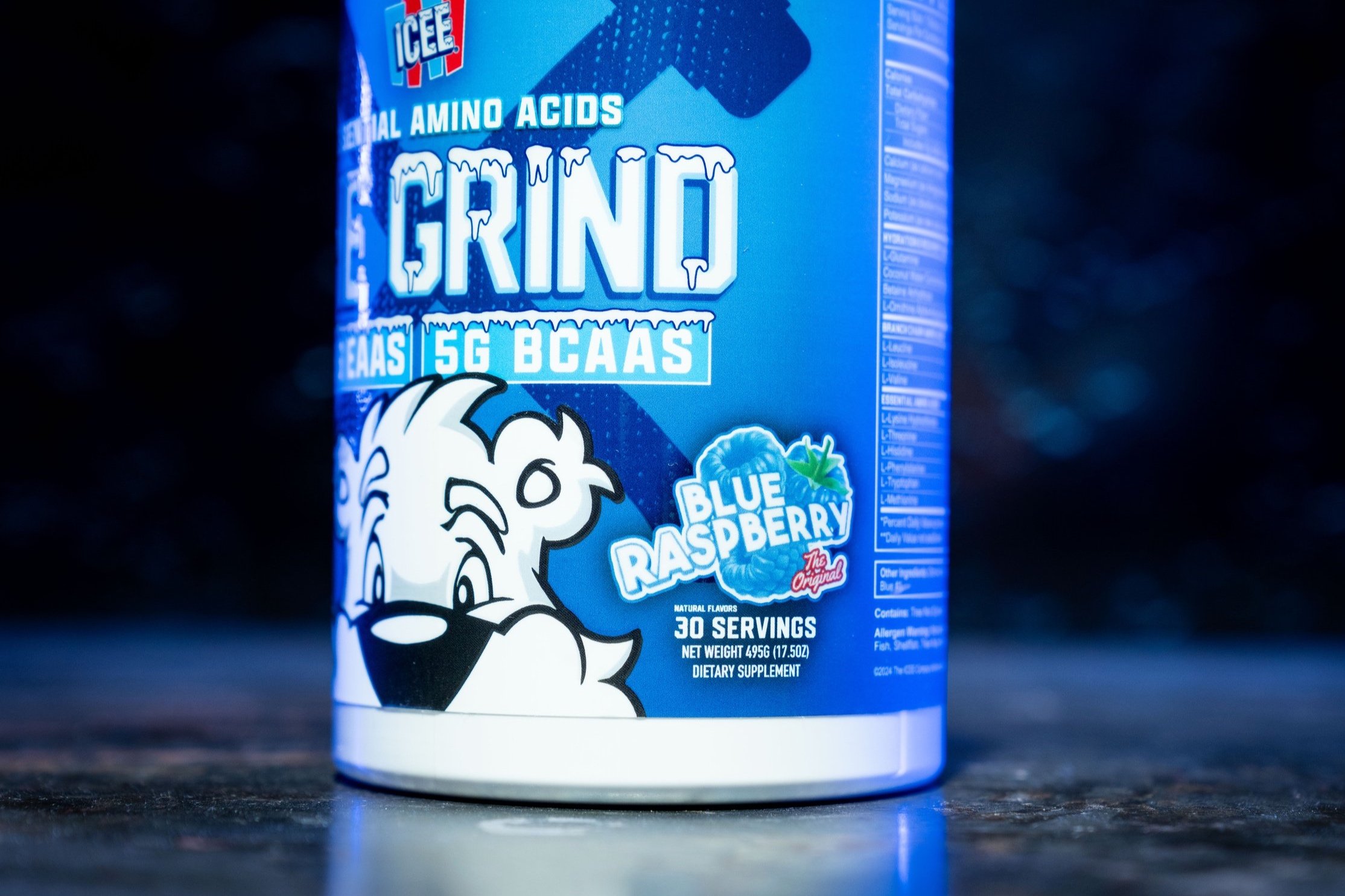 A blue container of dietary supplement with the label 'Grind' containing blue raspberry flavored amino acids, BCAAs, and electrolytes, showing cartoon animal mascot on the front and text indicating 30 servings and 495 grams net weight.