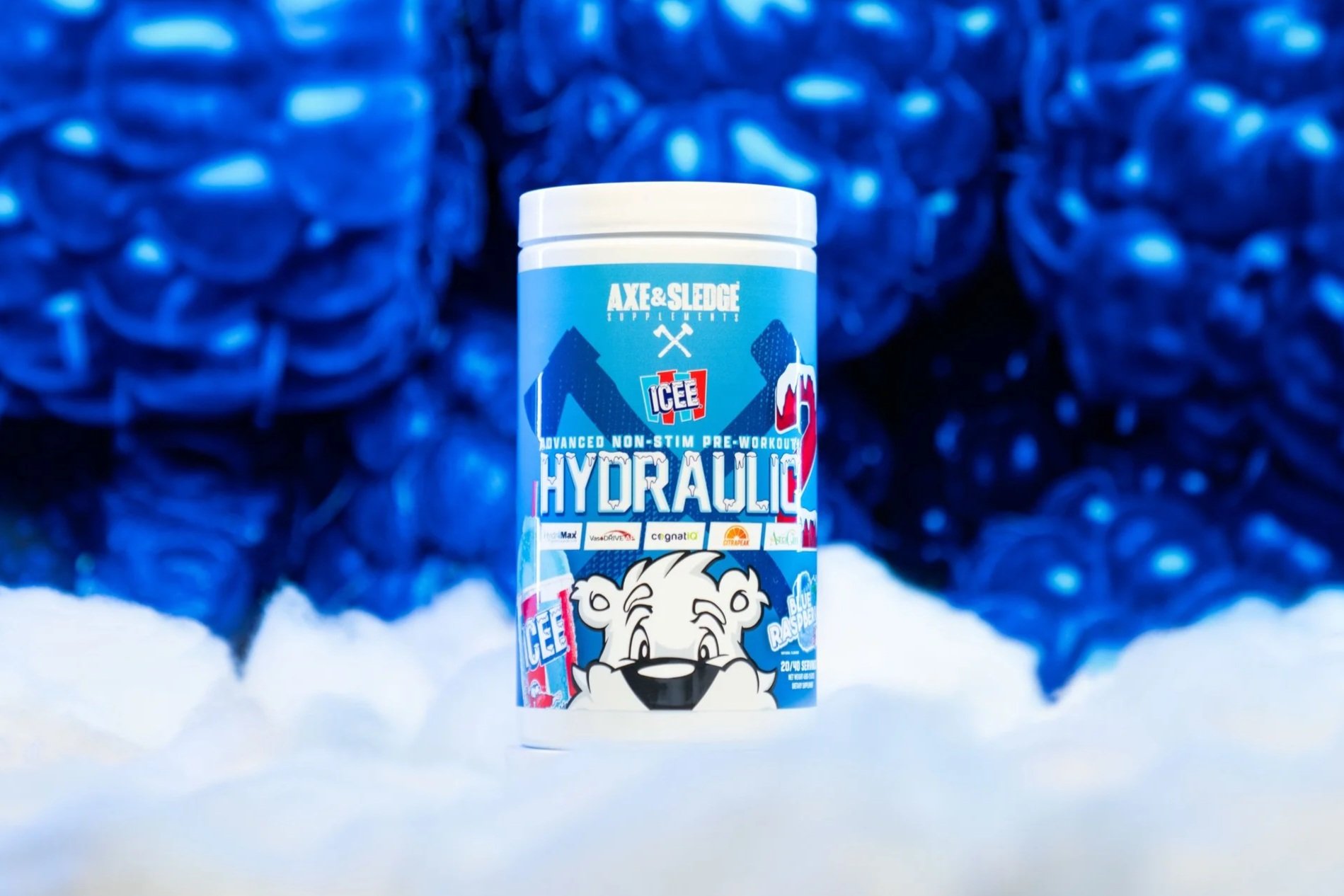 A container of ICEE Hydrolique pre-workout supplement with raspberry flavor, featuring a polar bear cartoon, placed on snow with blue balloons in the background.