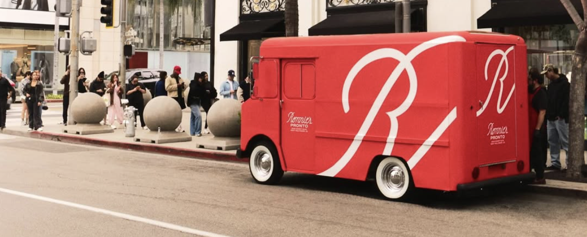 A small red delivery truck with white typography in a busy city street.