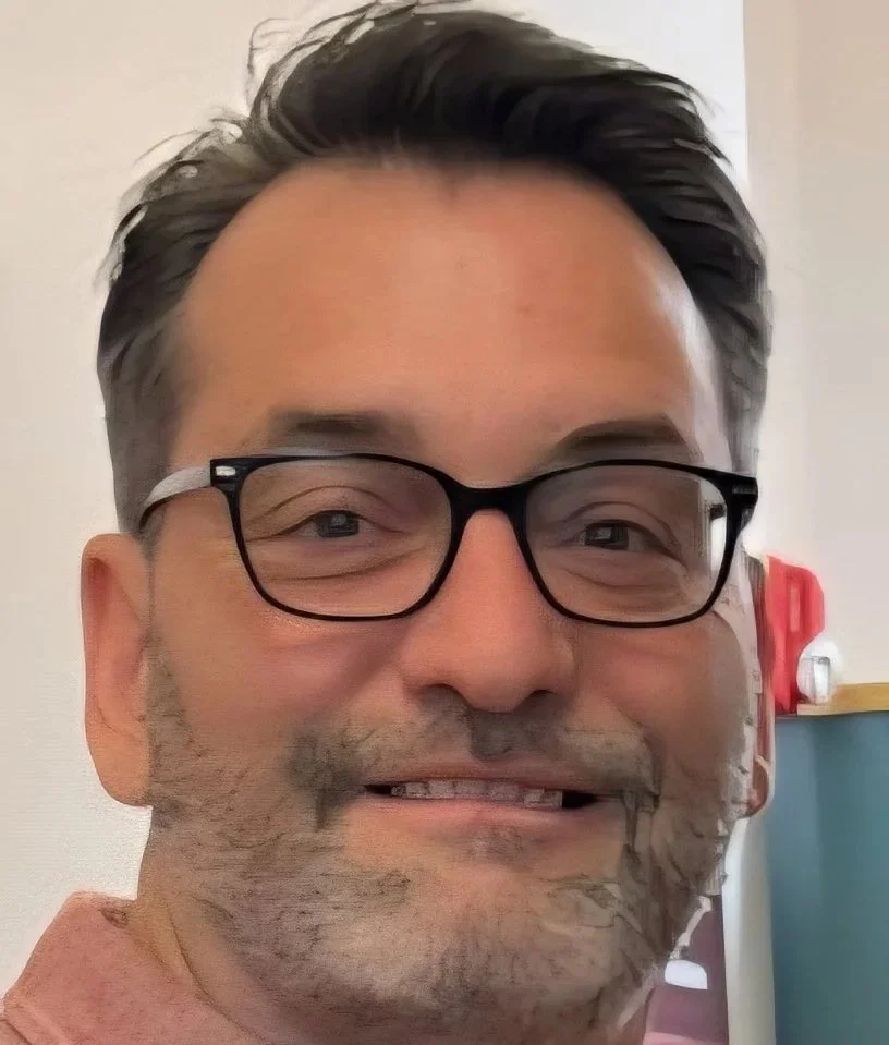 A person with light skin, glasses, and a white and black beard. 