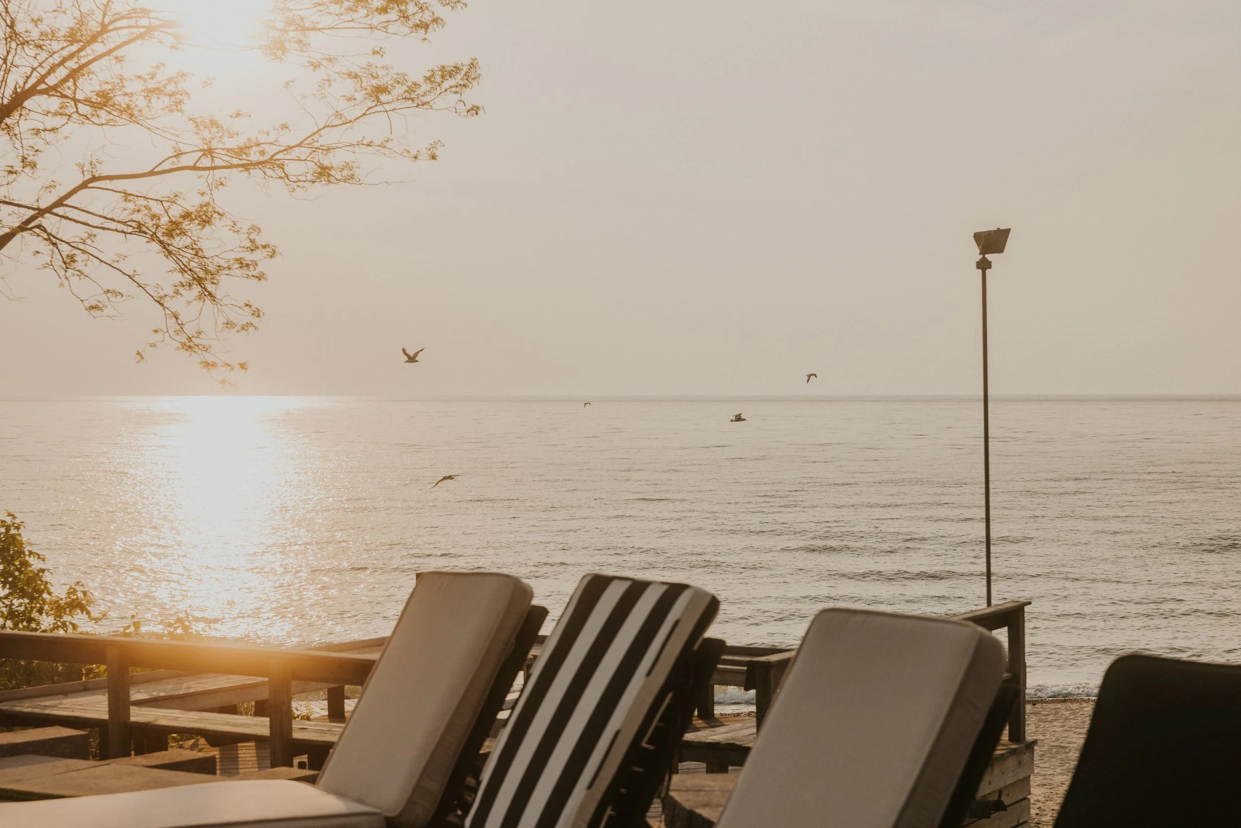 Striped lounge chairs on the deck facing a golden Lake Michigan sunset at Lighthouse Bluff