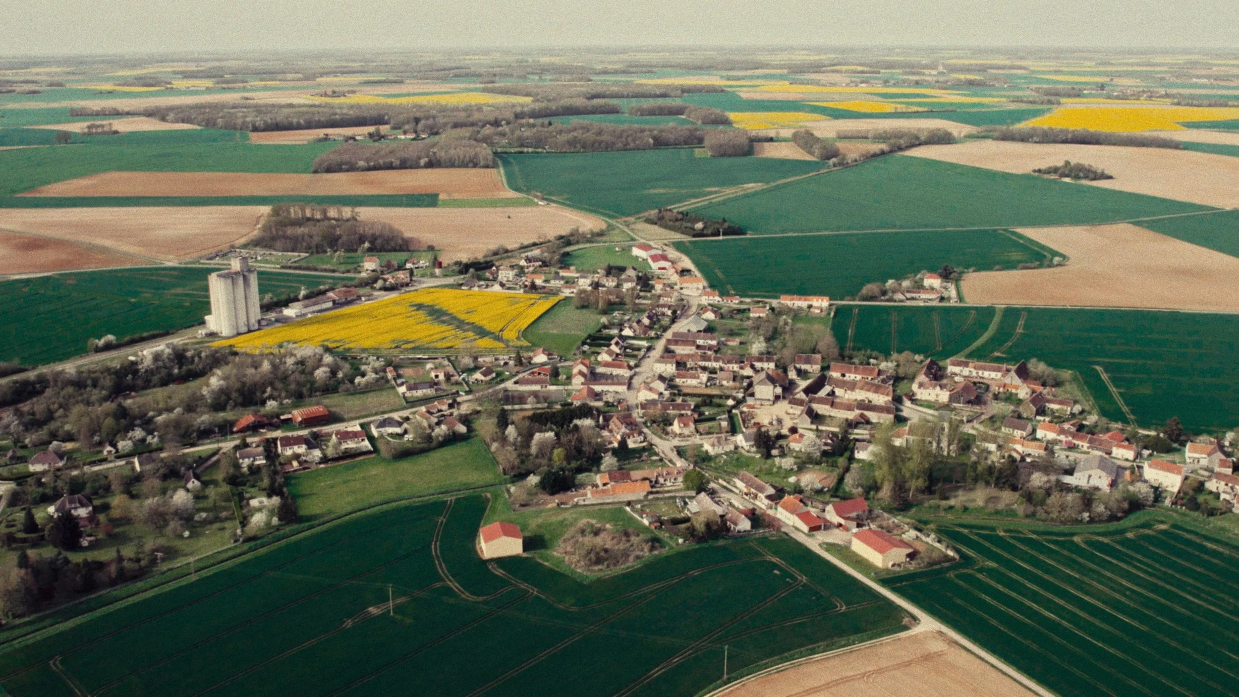 Aerial view of a small town surrounded by farmland and fields in various shades of green and yellow.