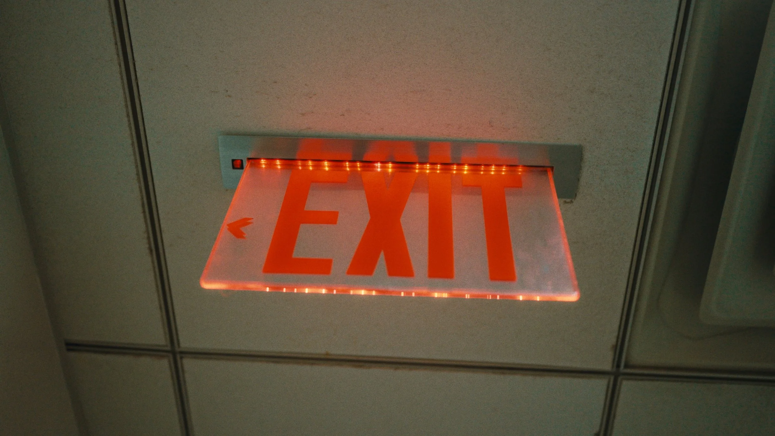 Illuminated red EXIT sign mounted on ceiling, with a left arrow.