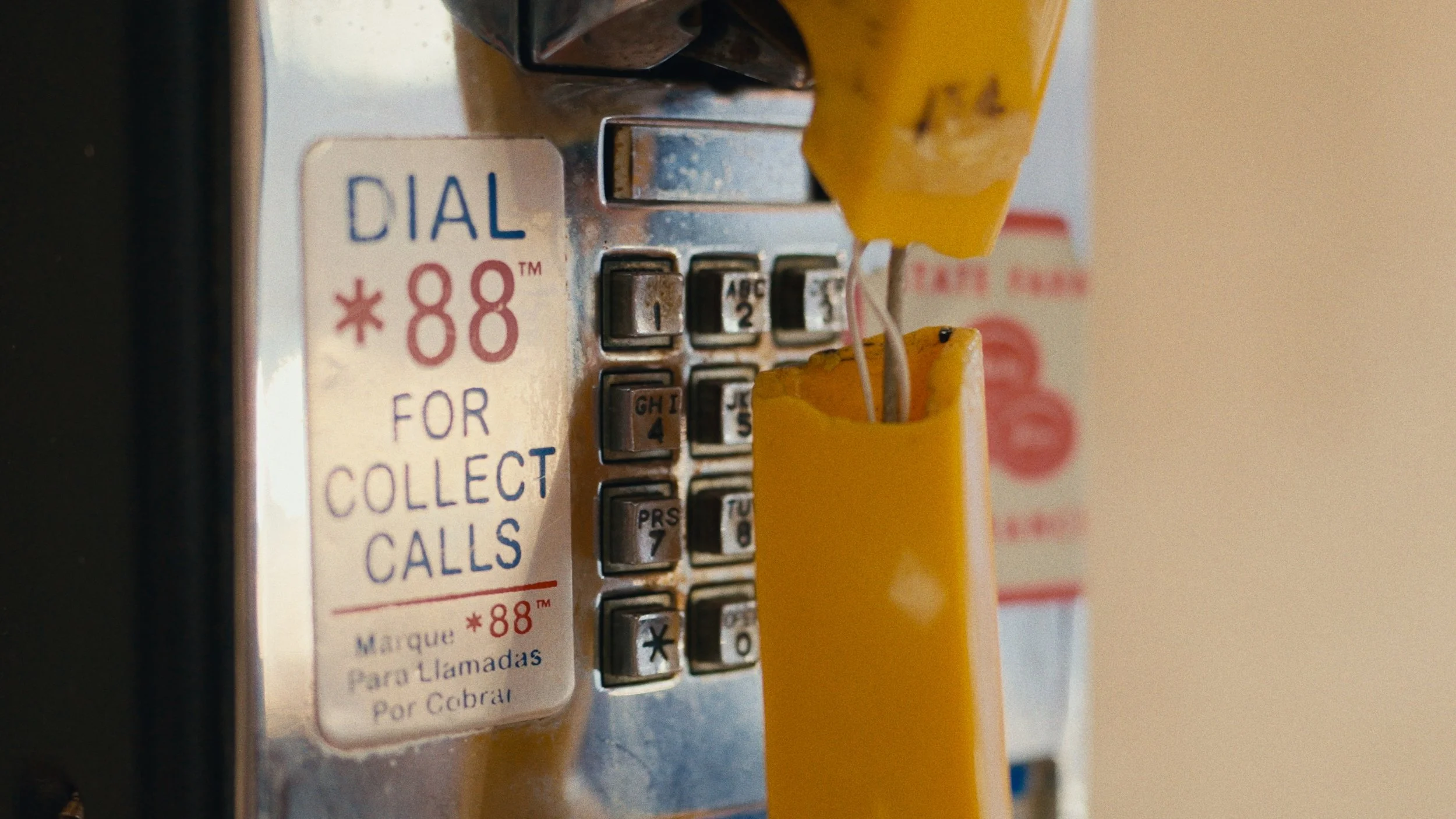 Close-up of a vintage payphone with a yellow handset hanging on the side and a sign instructing to dial *88 for collect calls.
