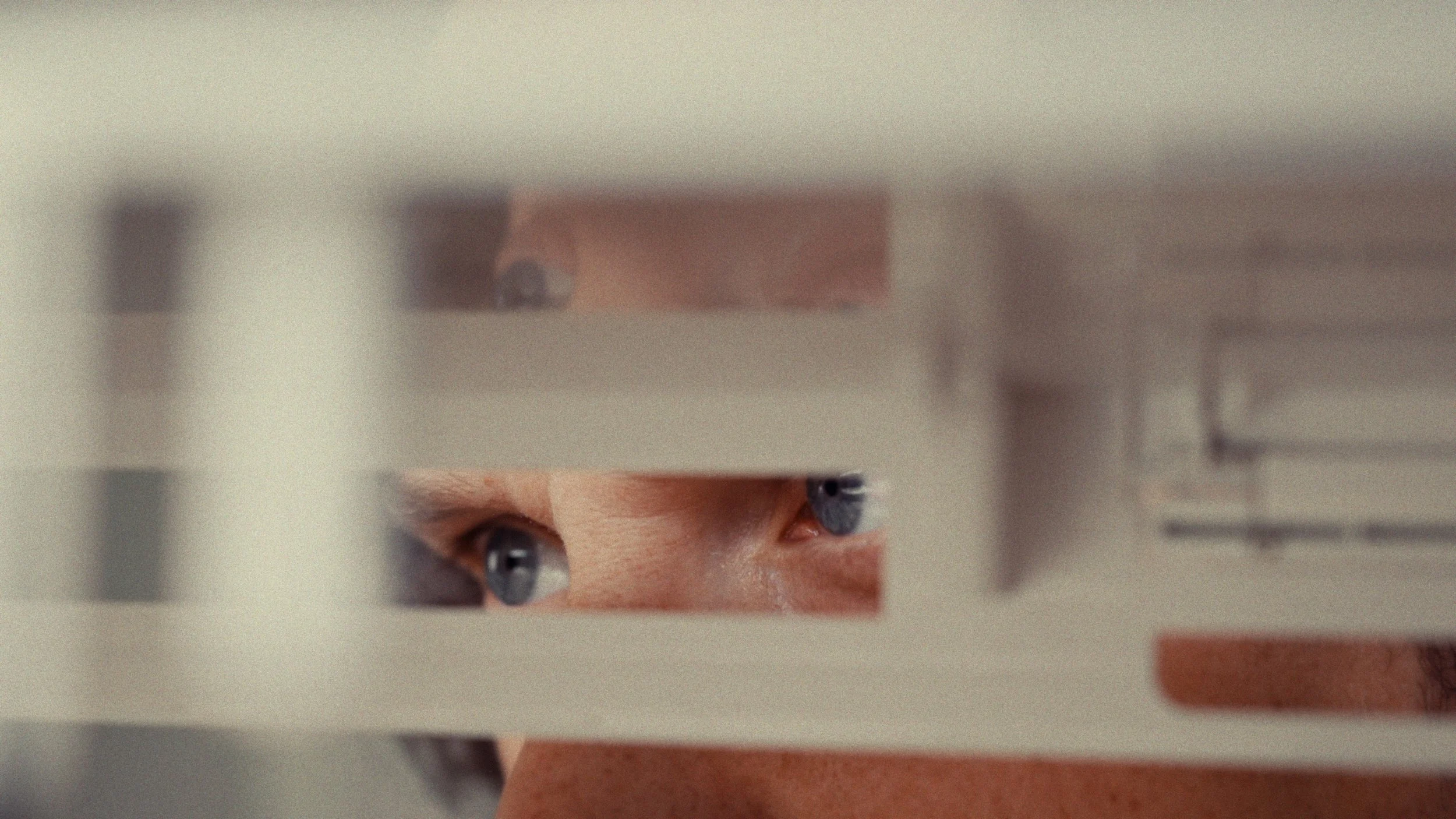 Close-up of a person's eyes seen through a small opening in a painted surface, looking intently.