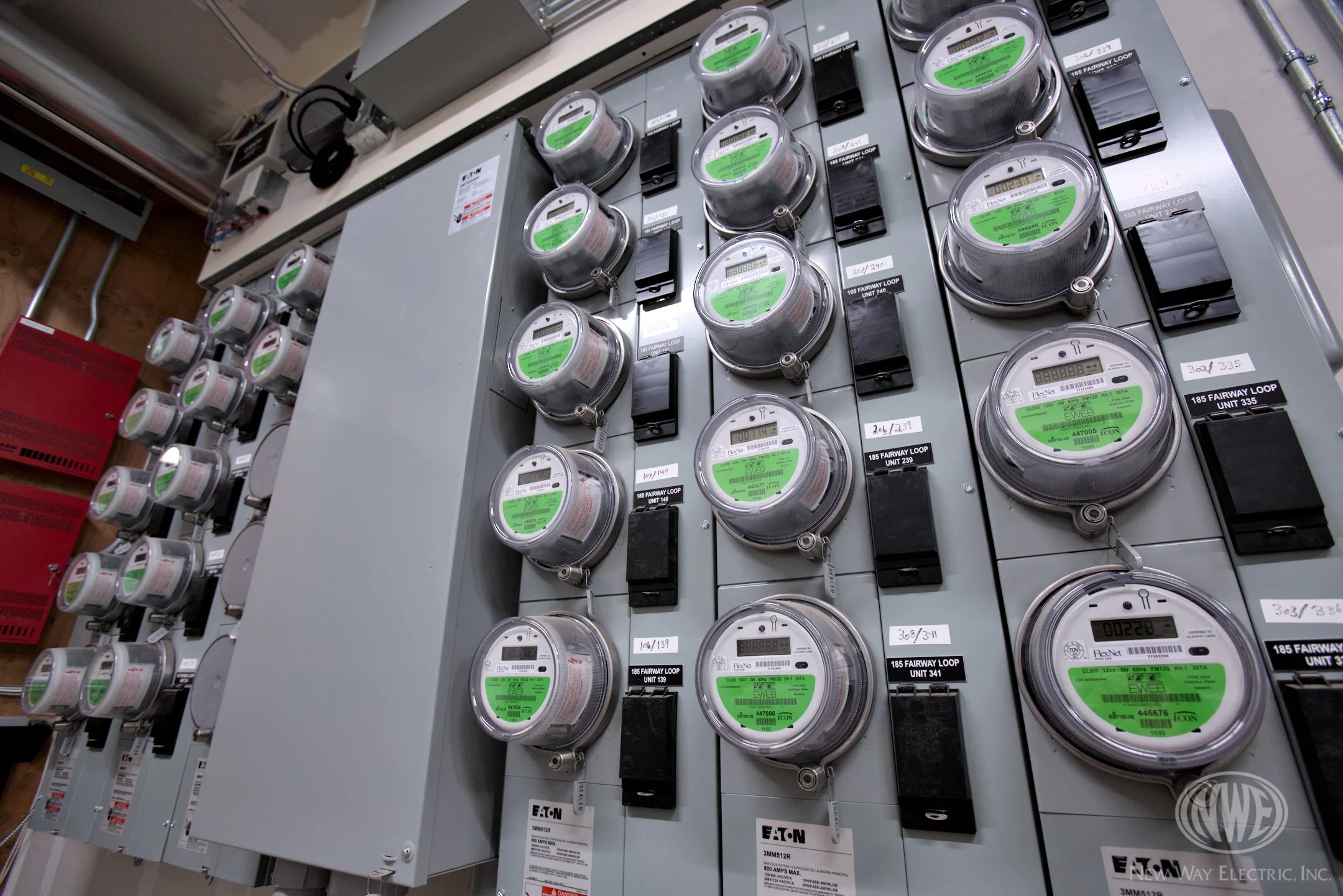 Electrical meters mounted on a panel, each with digital displays and green labels, in an industrial or utility setting.