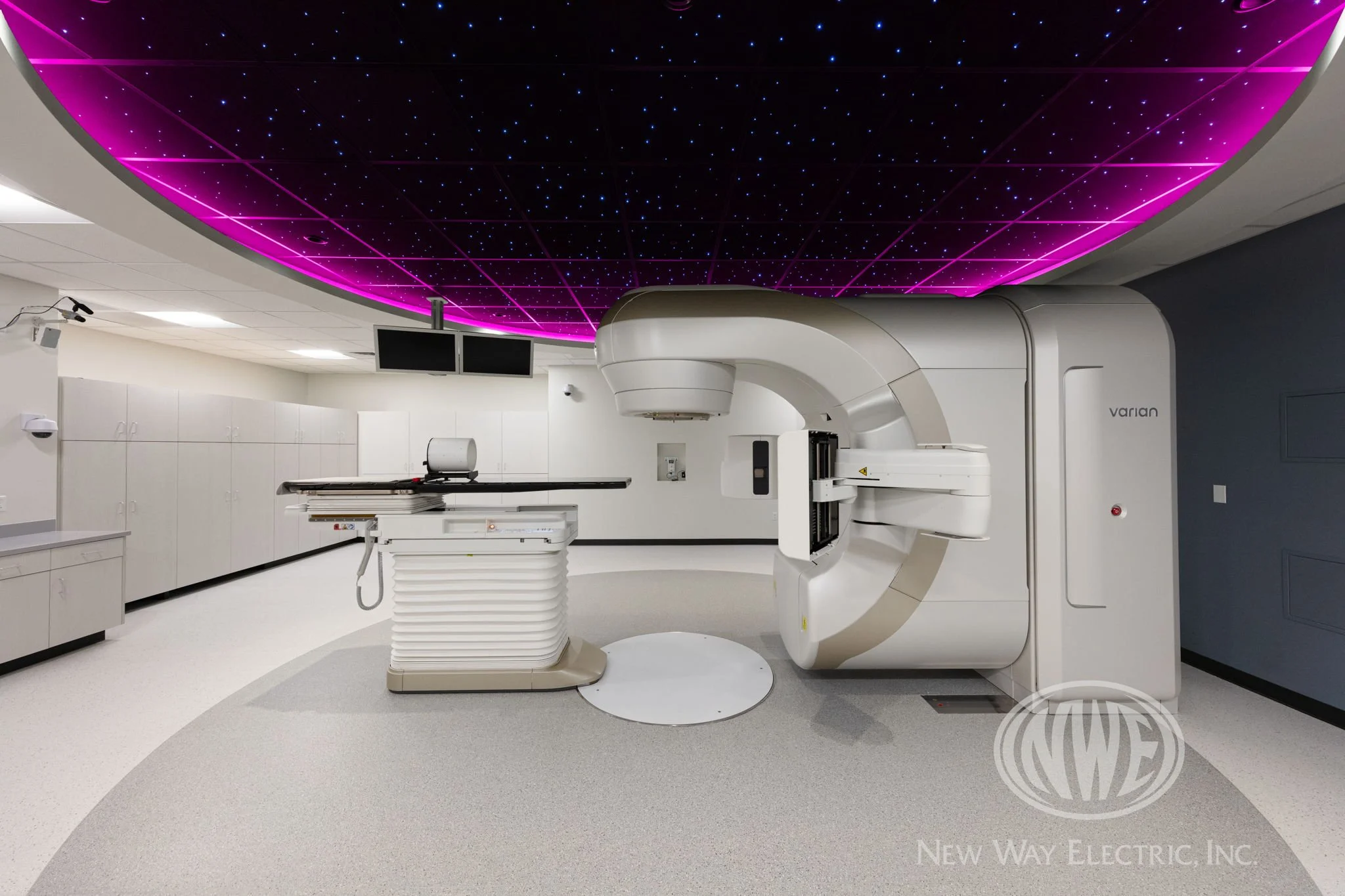 A modern medical imaging room with a large CT scanner and a digitally illuminated ceiling with pink and purple lighting.