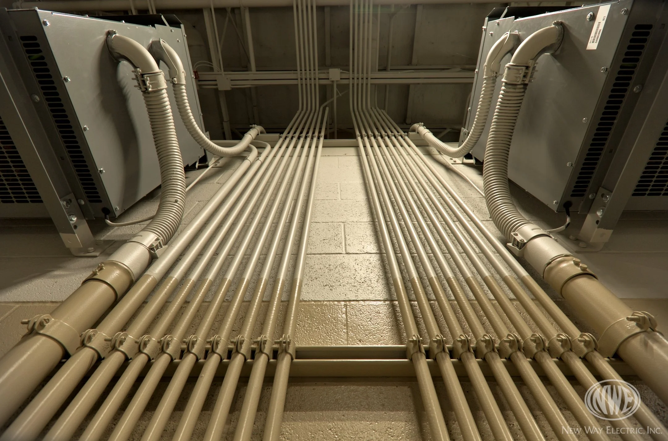 Electrical conduit pipes and panels installed on a ceiling and wall in an industrial or electrical room.
