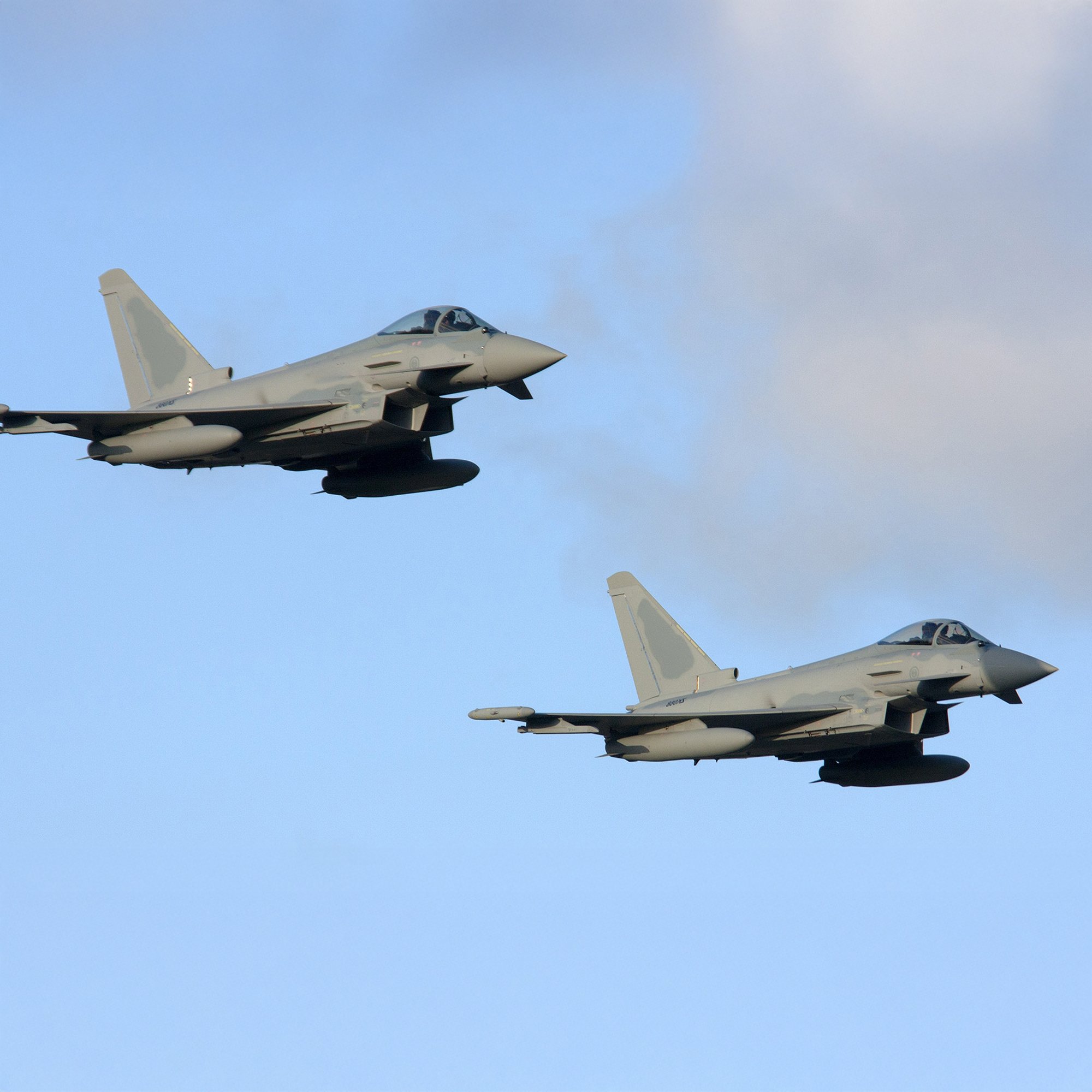 Two fighter jets flying in formation against a partly cloudy sky.