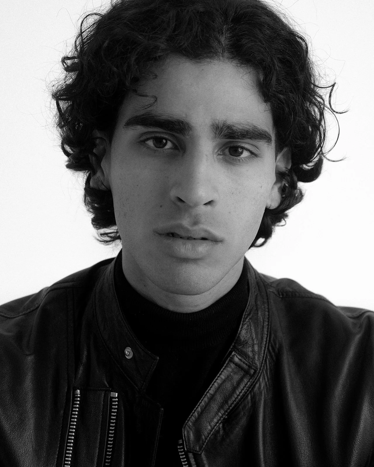 Close-up black and white portrait of a young man with curly hair wearing a leather jacket.
