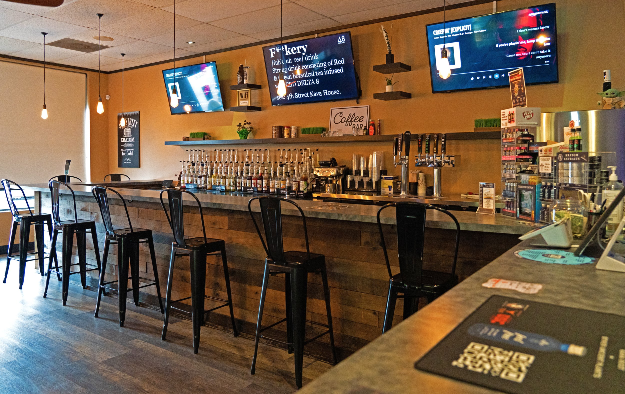 Inside a bar with a counter, black chairs, and digital screens on the wall.