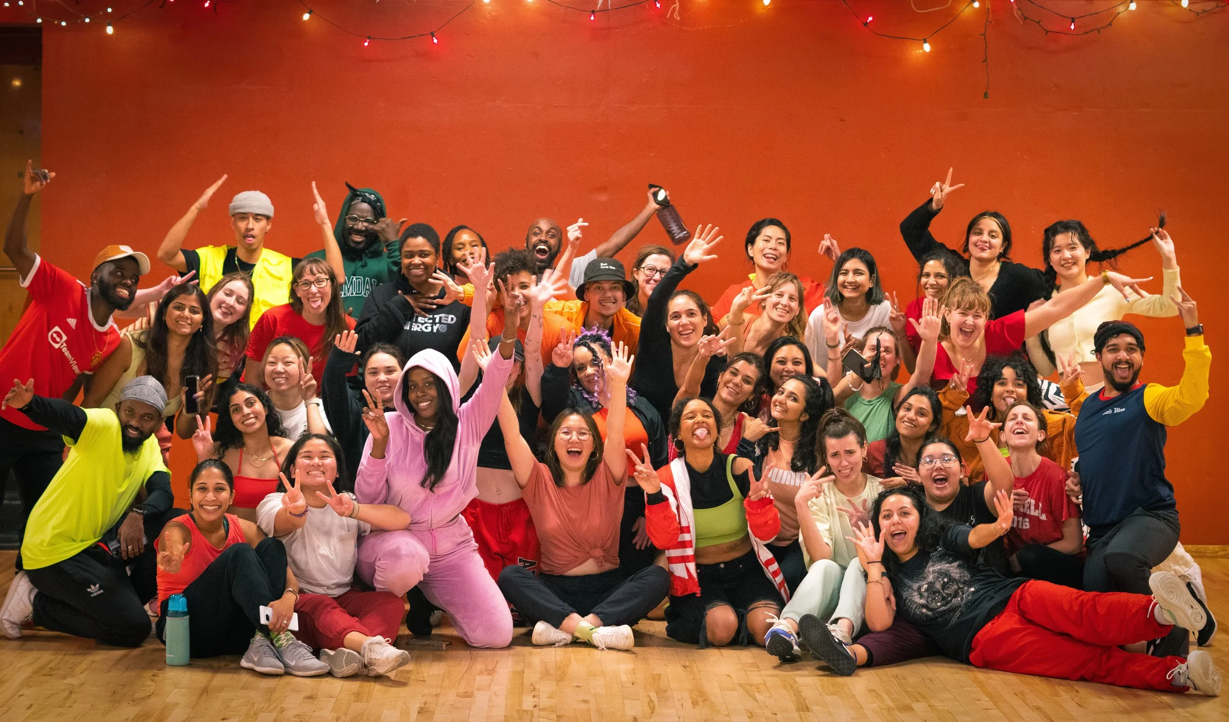 A group of people dancing together at a party or dance event, with a woman wearing a black face mask and a black crop top leading closely behind a man in a black sports jersey and patterned pants. Afro dancing at Dance Underground in Capitol Hill.