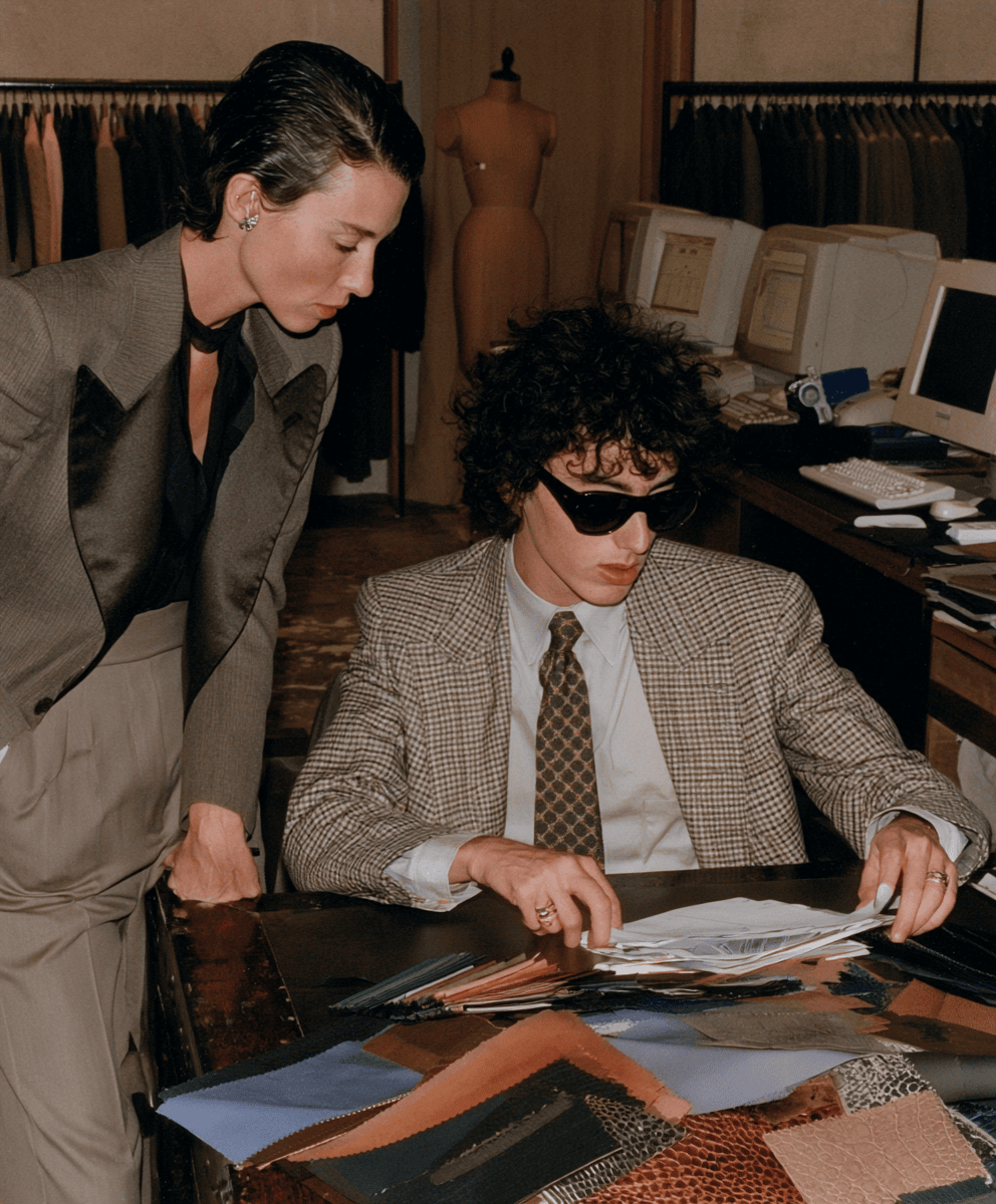 Person in a plaid suit looking though fabric samples on a table, with suit displays in the background.