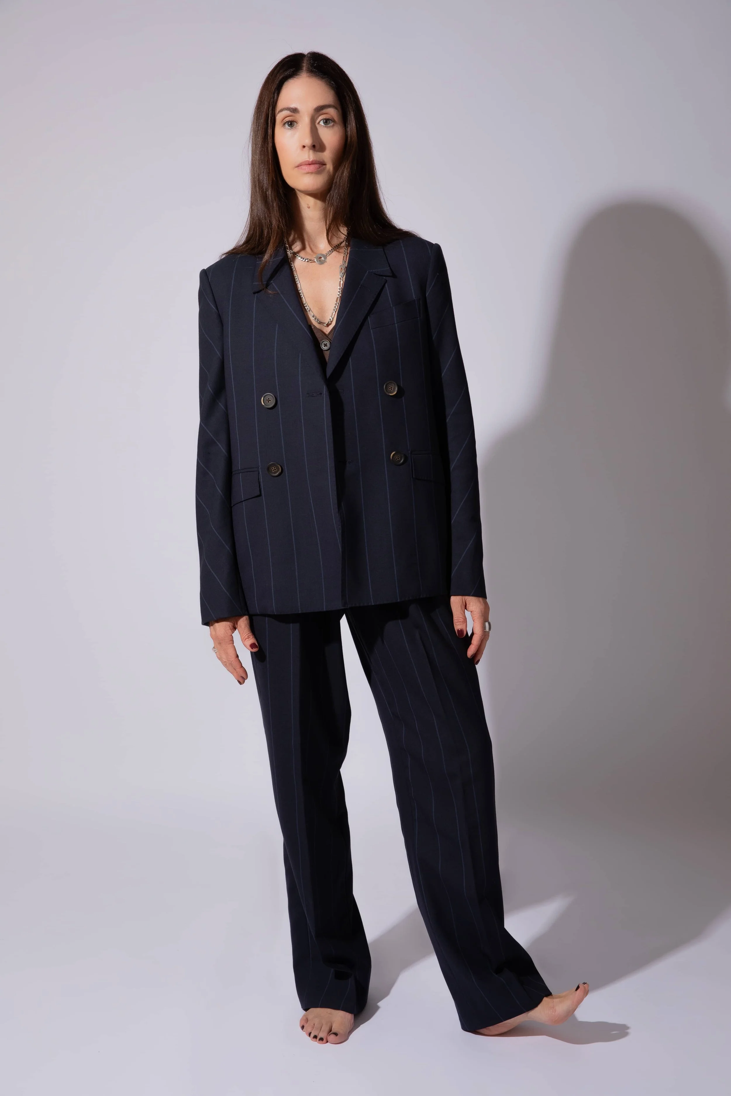 A woman wearing a custom women's suit in navy pinstripe double-breasted suit with pleated pants on a neutral gray background.