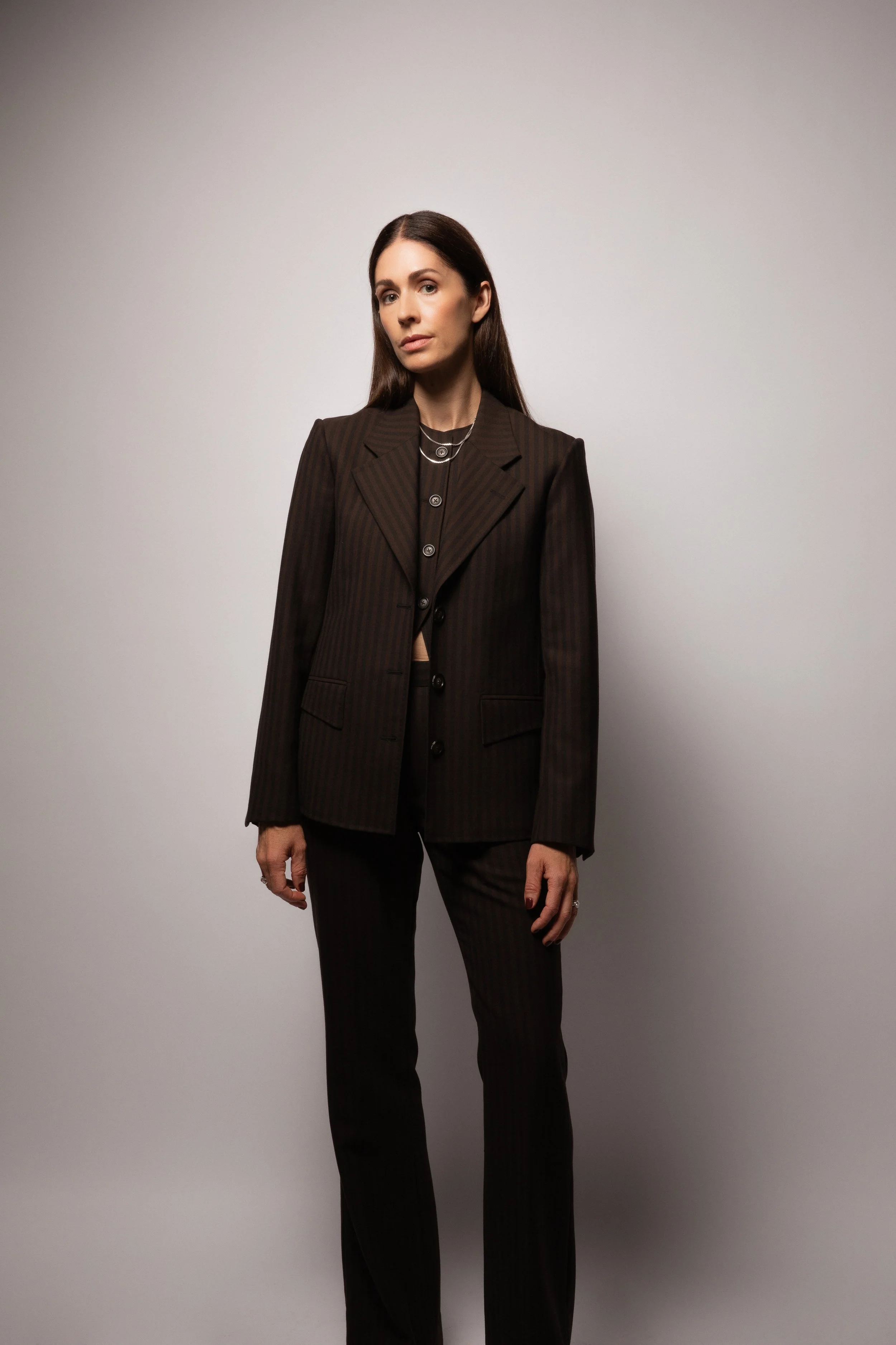 A woman wearing a custom women's 3 piece suit in a dark brown and black stripe high neck vest