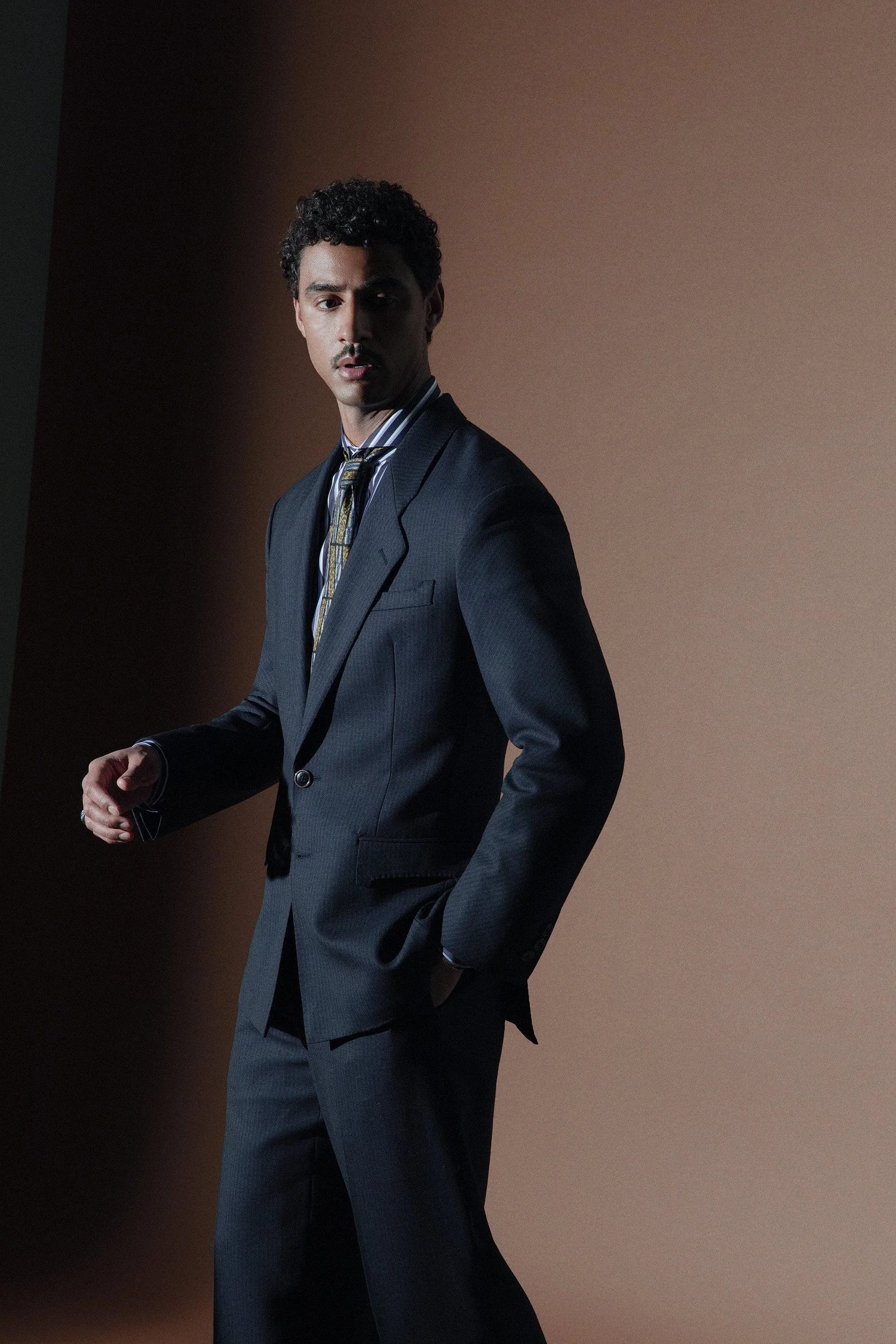 Our most classic silhouette. The jacket is longer and has wide shoulders with a nipped waist and a more relaxed pant. Made in a Dugdale tropical cloth in blue and black shadow stripes.