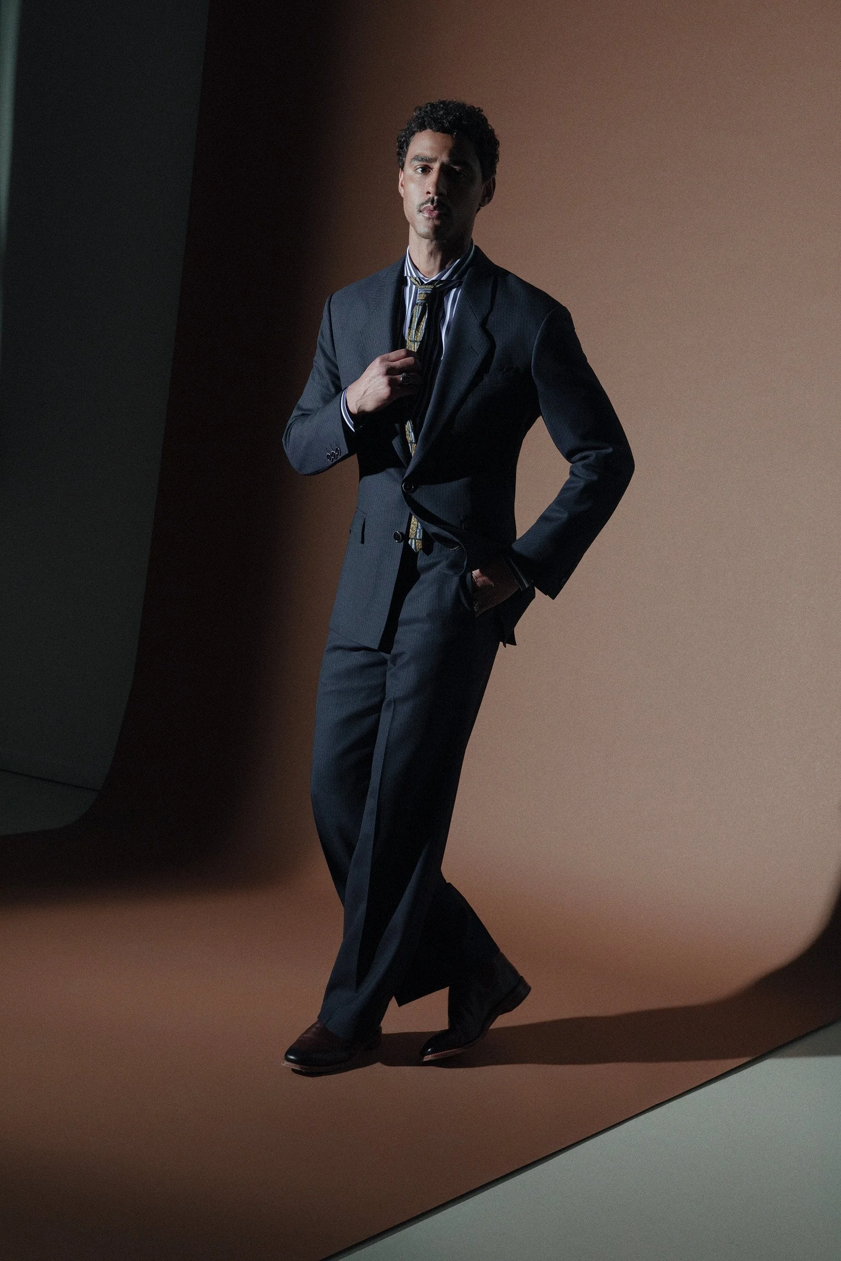 Our most classic silhouette. The longer jacket, wide shoulders and nipped waist with the more relaxed pant evokes an array of era's from the 20's,40's, and 80's. Made in a Dugdale tropical cloth in blue and black shadow stripes.