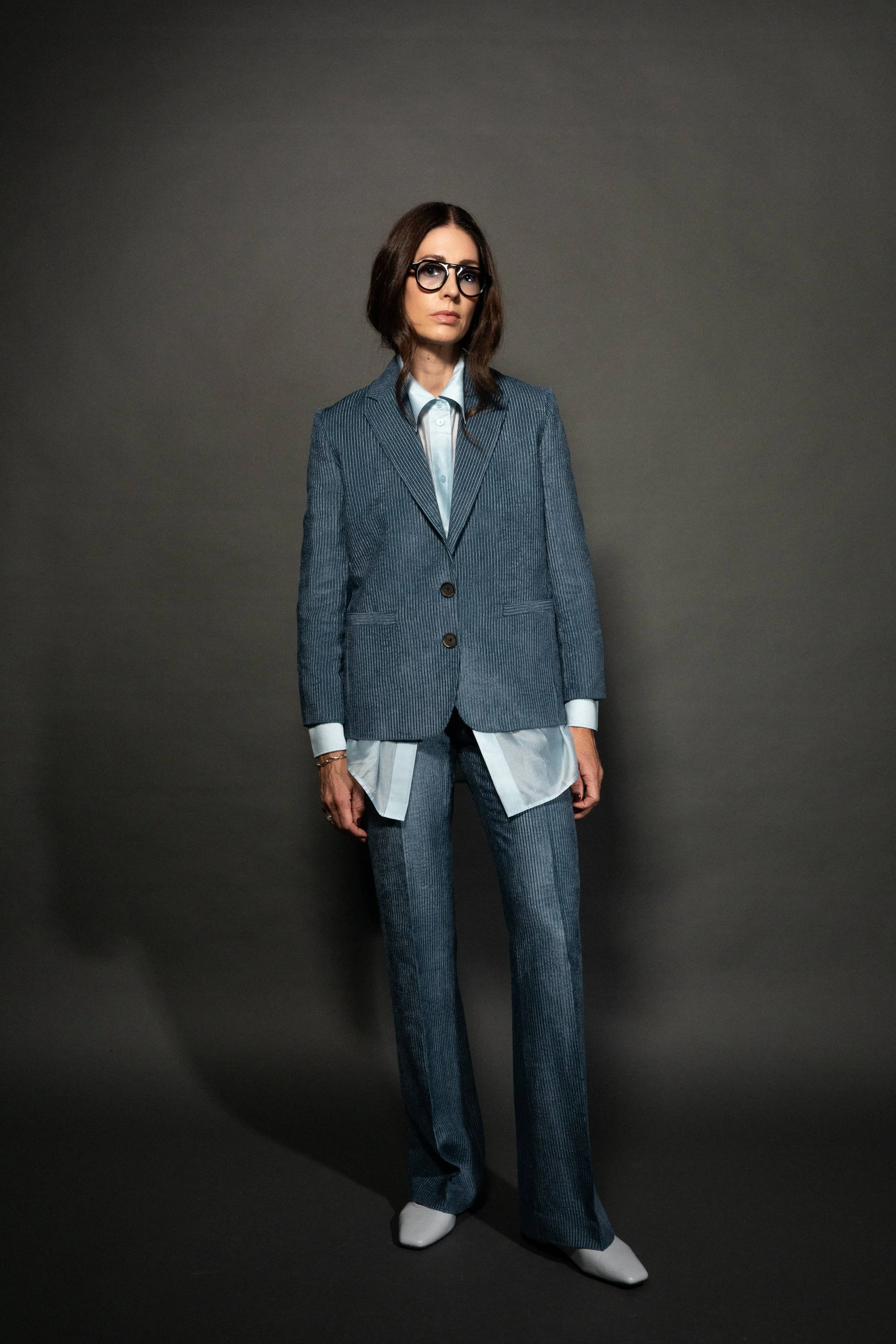 Nonbinary Person in glasses wearing a denim blue corduroy suit