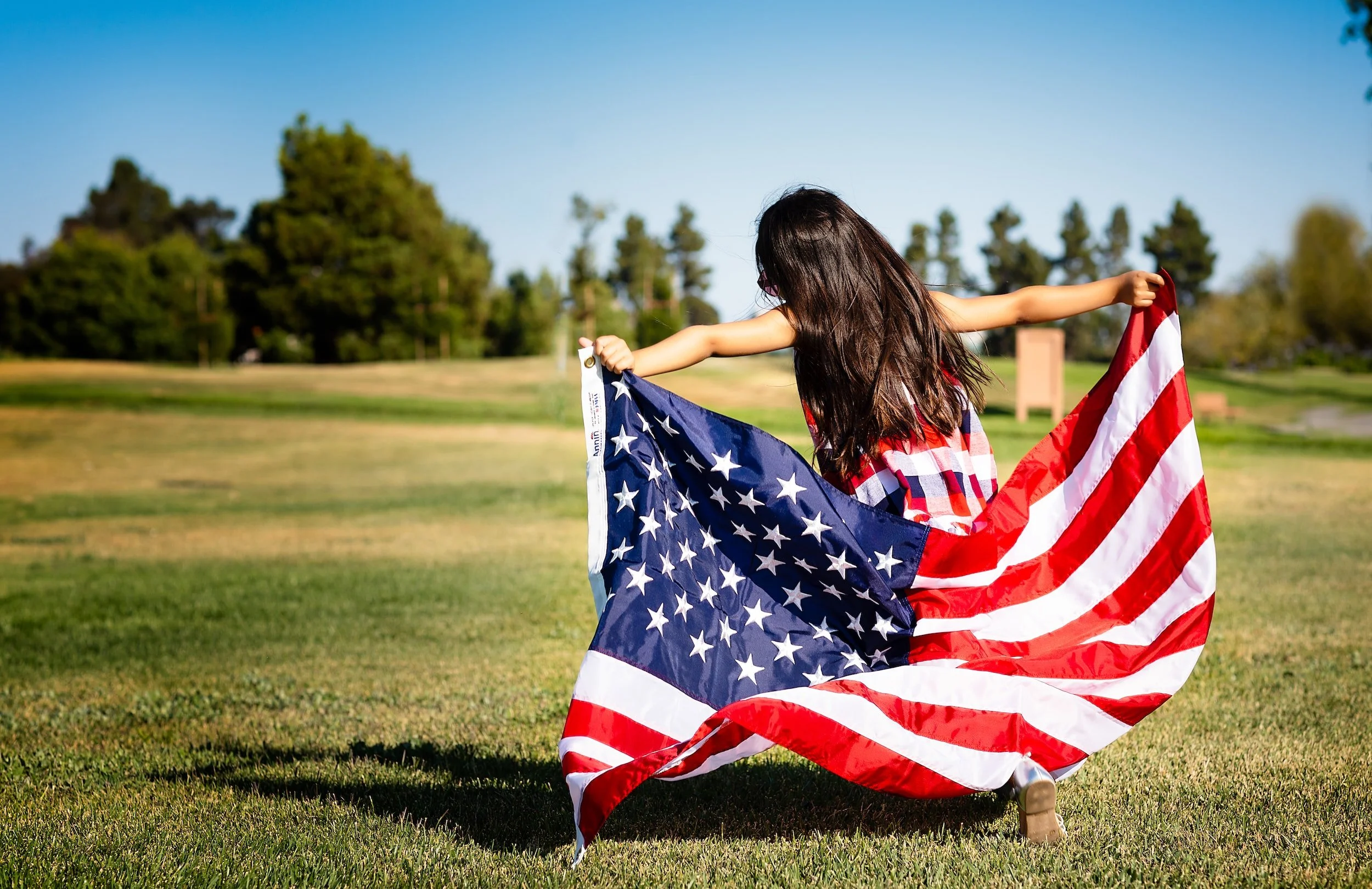 A young girl running across a field holding an American flag