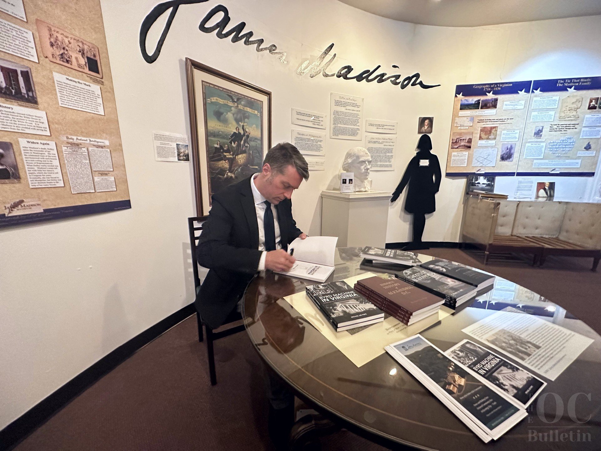  Award-winning journalist and author Michael Lee Pope signs a copy of his book at the James Madison Museum on Sunday, April 16. (Photo Credit: Adam Belmar) 
