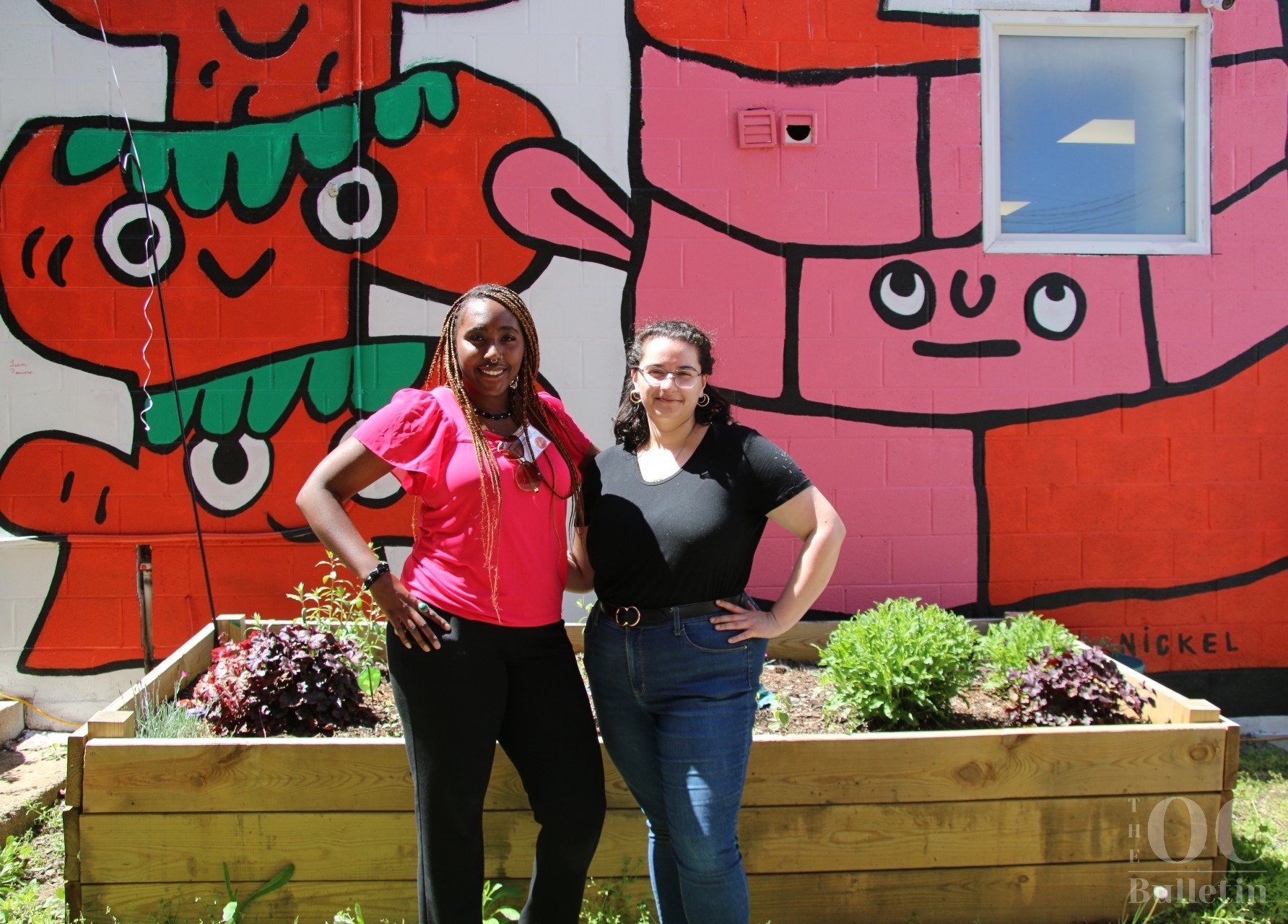  From left to right: Arts center administrative assistant Cheylyn Grant and program coordinator Laura Link stand in the community garden located behind the building. (Photo Credit: Andra Landi) 