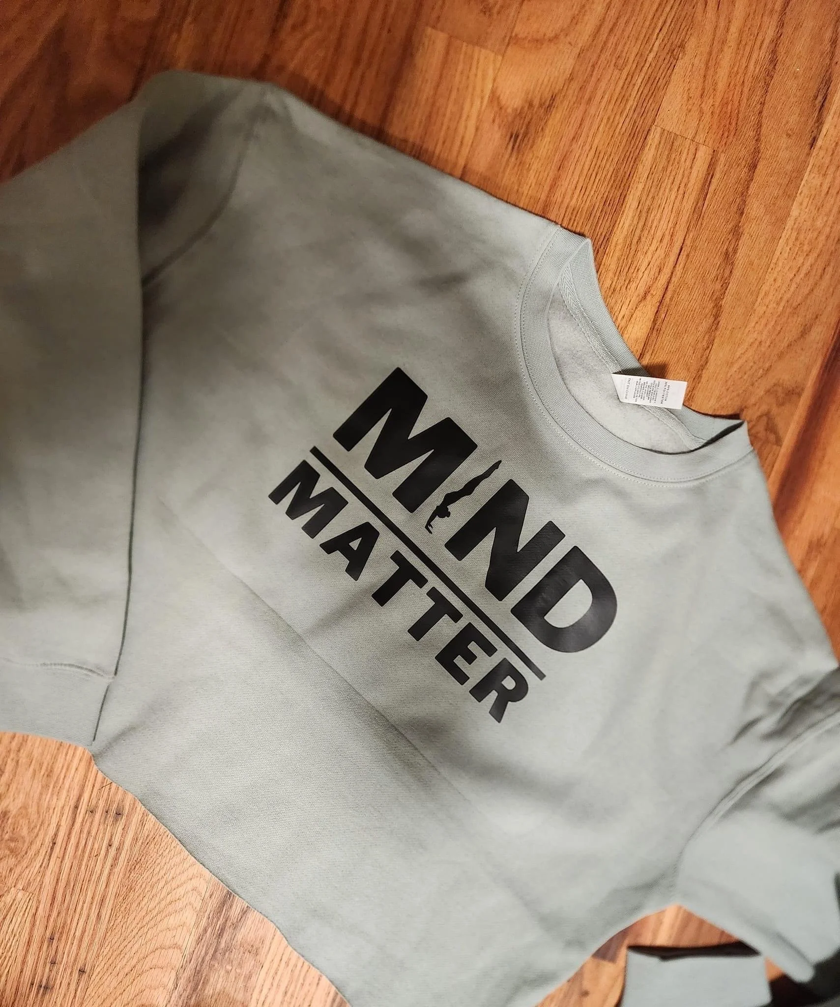 Light gray sweatshirt with bold black text that reads "MIND MATTER" placed on a wooden floor.