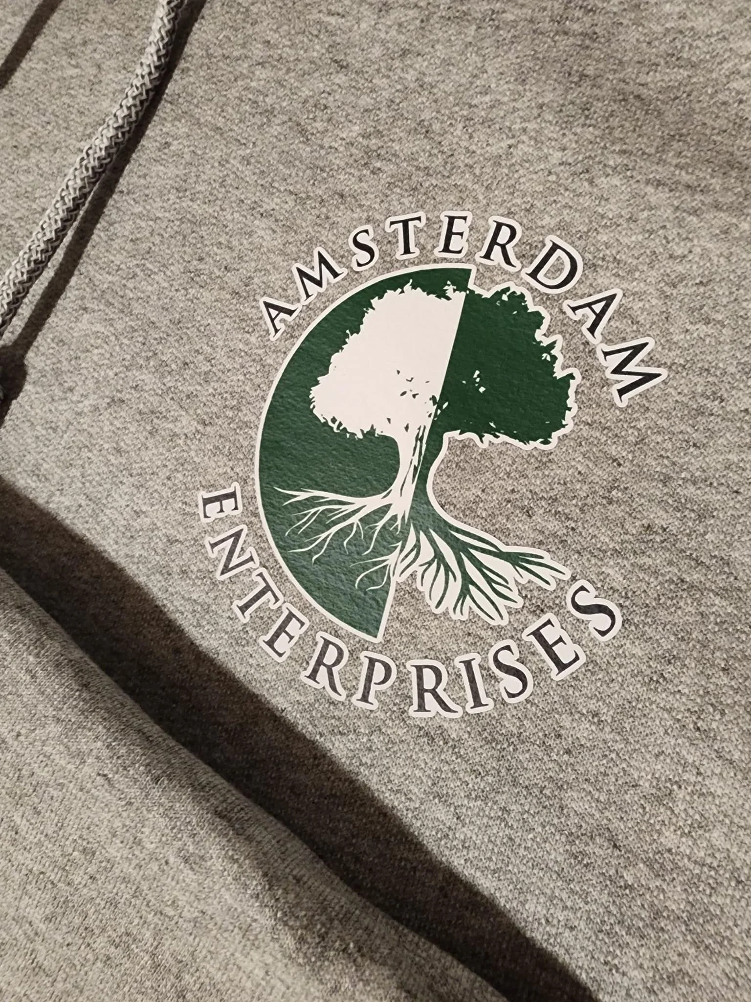 A gray hoodie with a logo of a tree and the words 'Amsterdam Enterprises' printed around it.