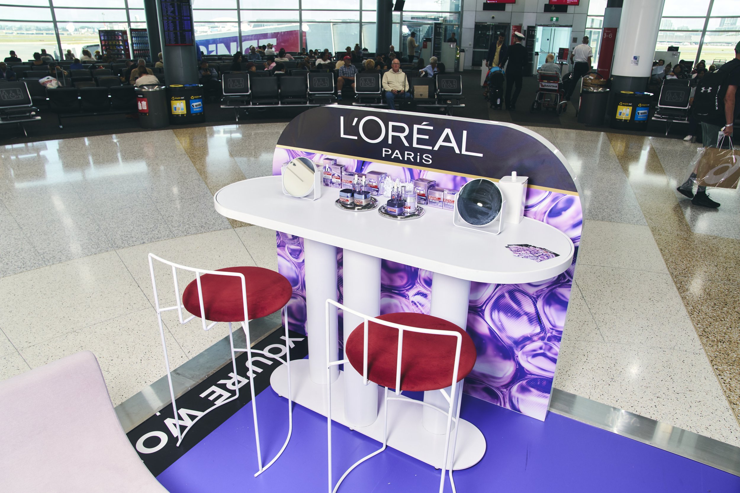 L'Oreal Paris promotional display in an airport waiting area with two red velvet chairs, mirrors, and skincare products
