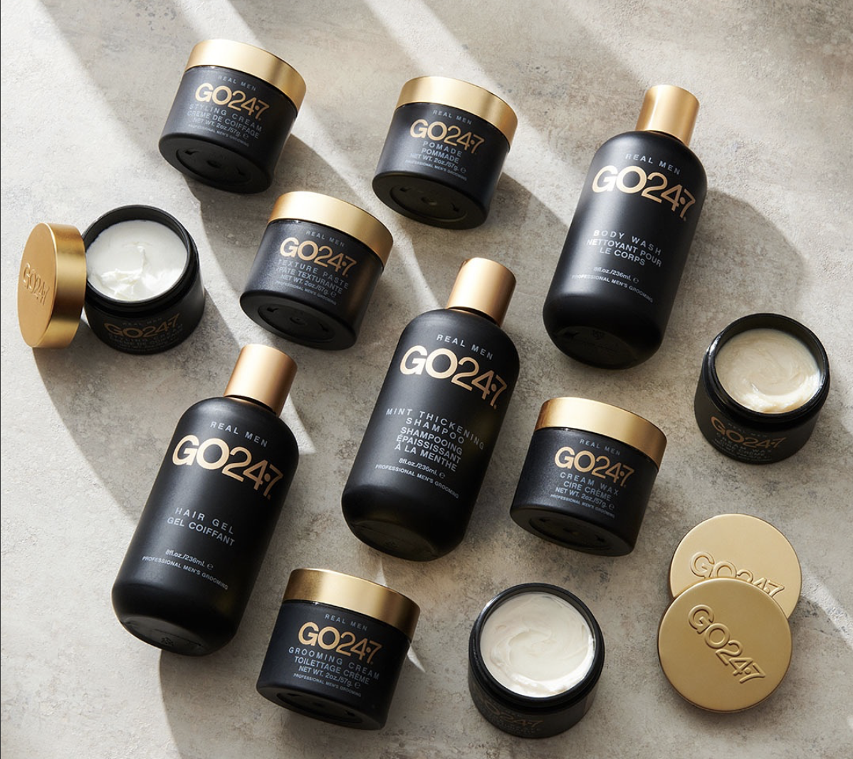 Collection of black and gold men's grooming products  from the brand GO247 including creams, gels, shampoos, and body wash on a light surface.