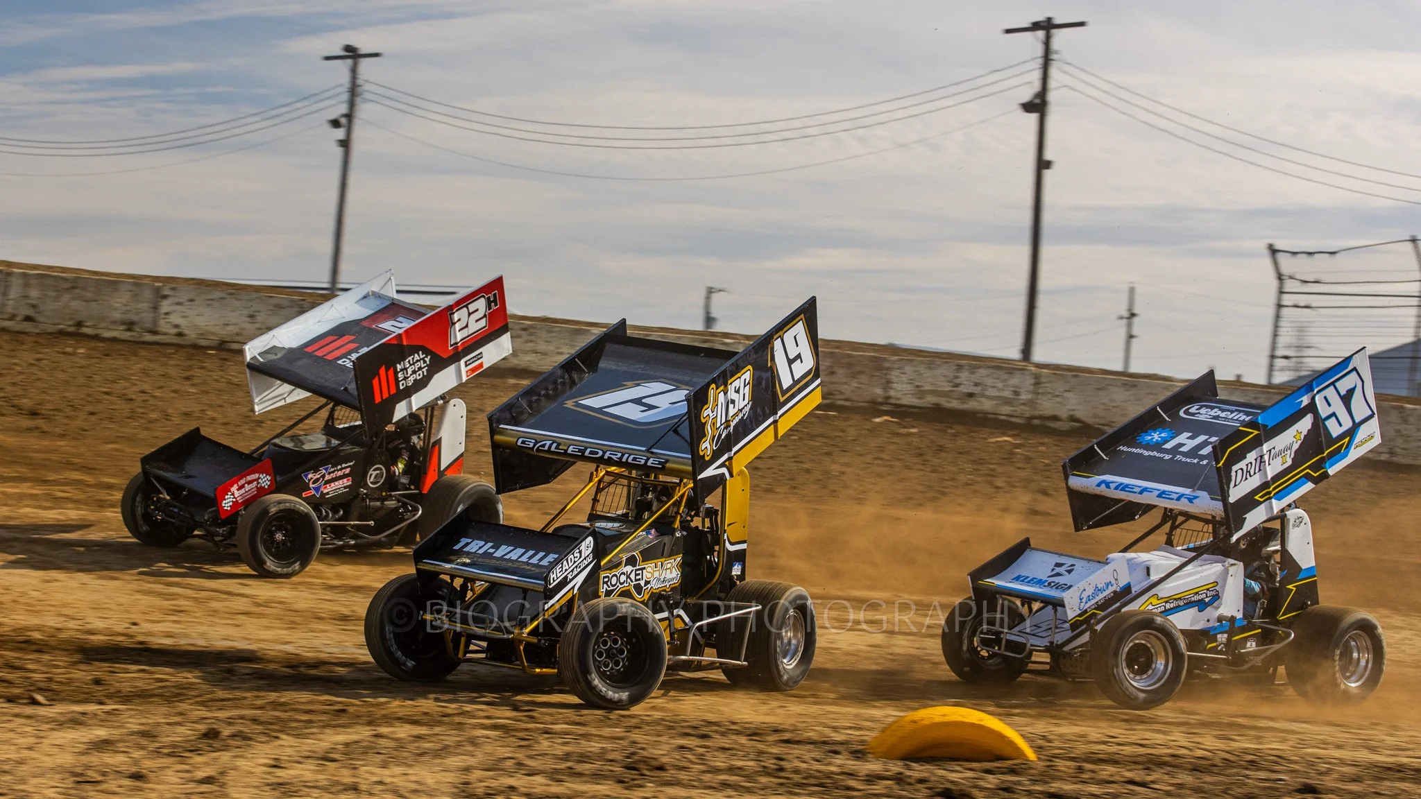 an image taken by a professional motorsport photographer of three sprint cars racing on a dirt track in Indianapolis
