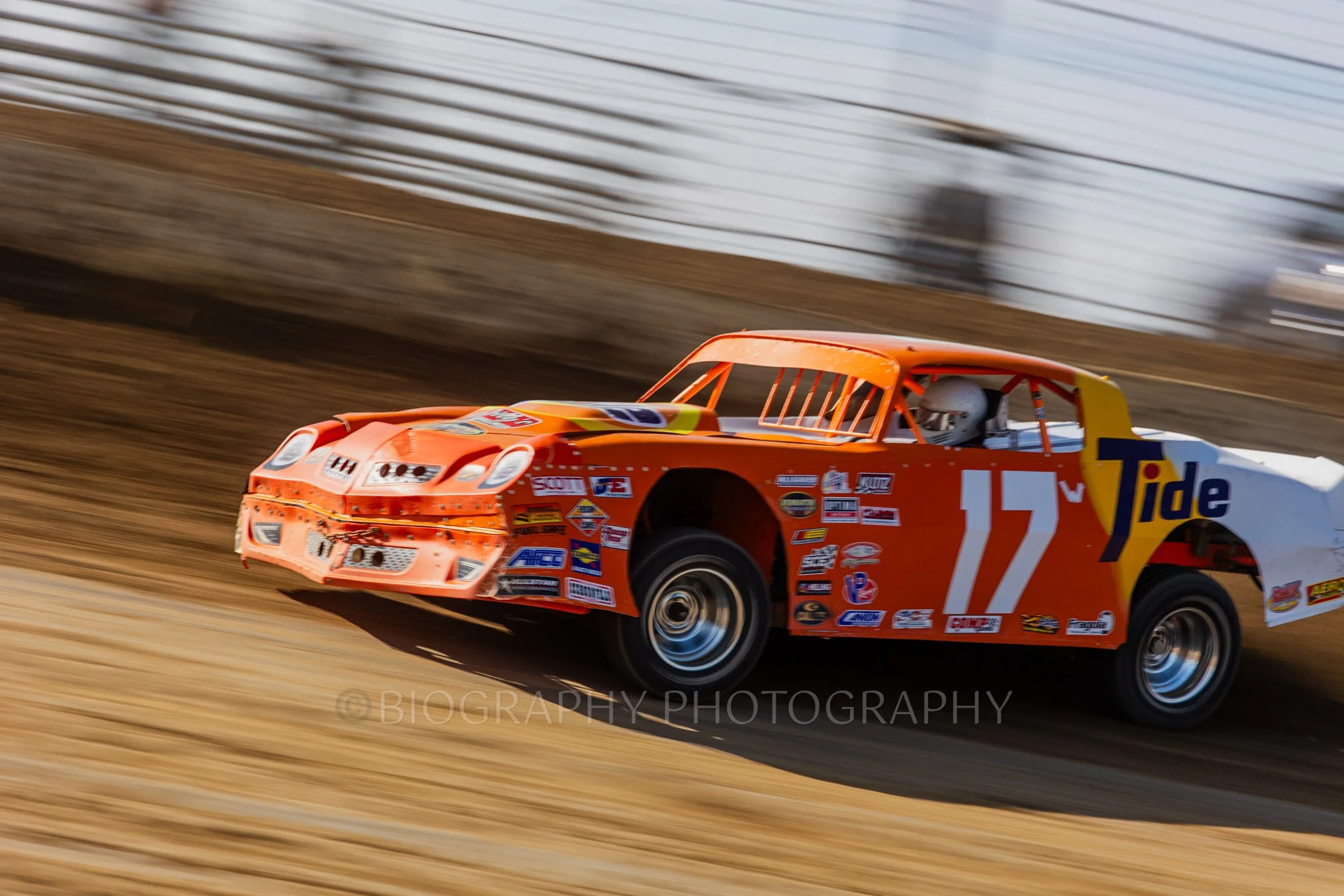 An image of an orange race car in the street stock category racing on a dirt track in Indianapolis, IN taken by a professional motorsport photographer