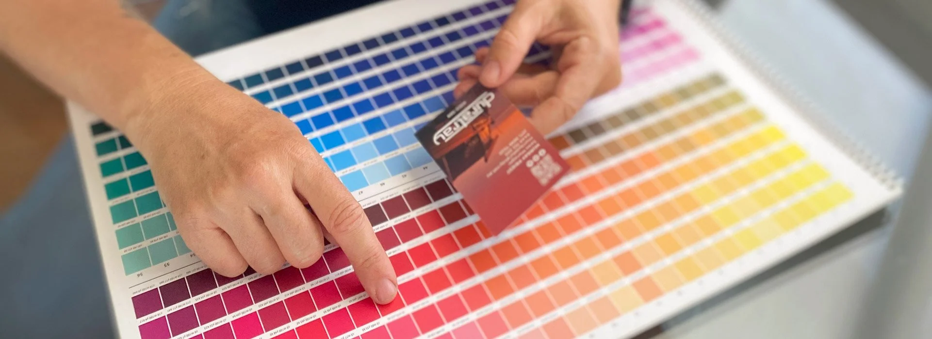 Designer comparing red colour swatches on a Pantone chart while holding a printed sample card, assessing print accuracy and colour matching.