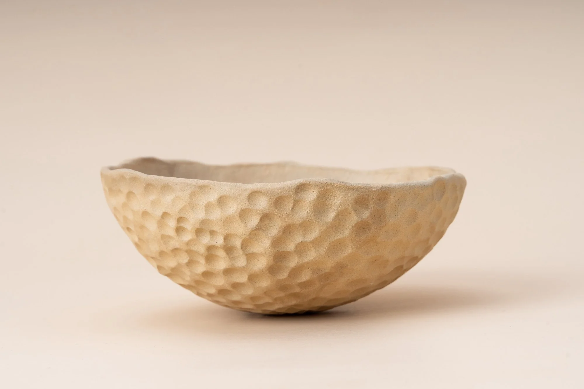 Cream-colored ceramic bowl with textured, dimpled surface on a neutral background.