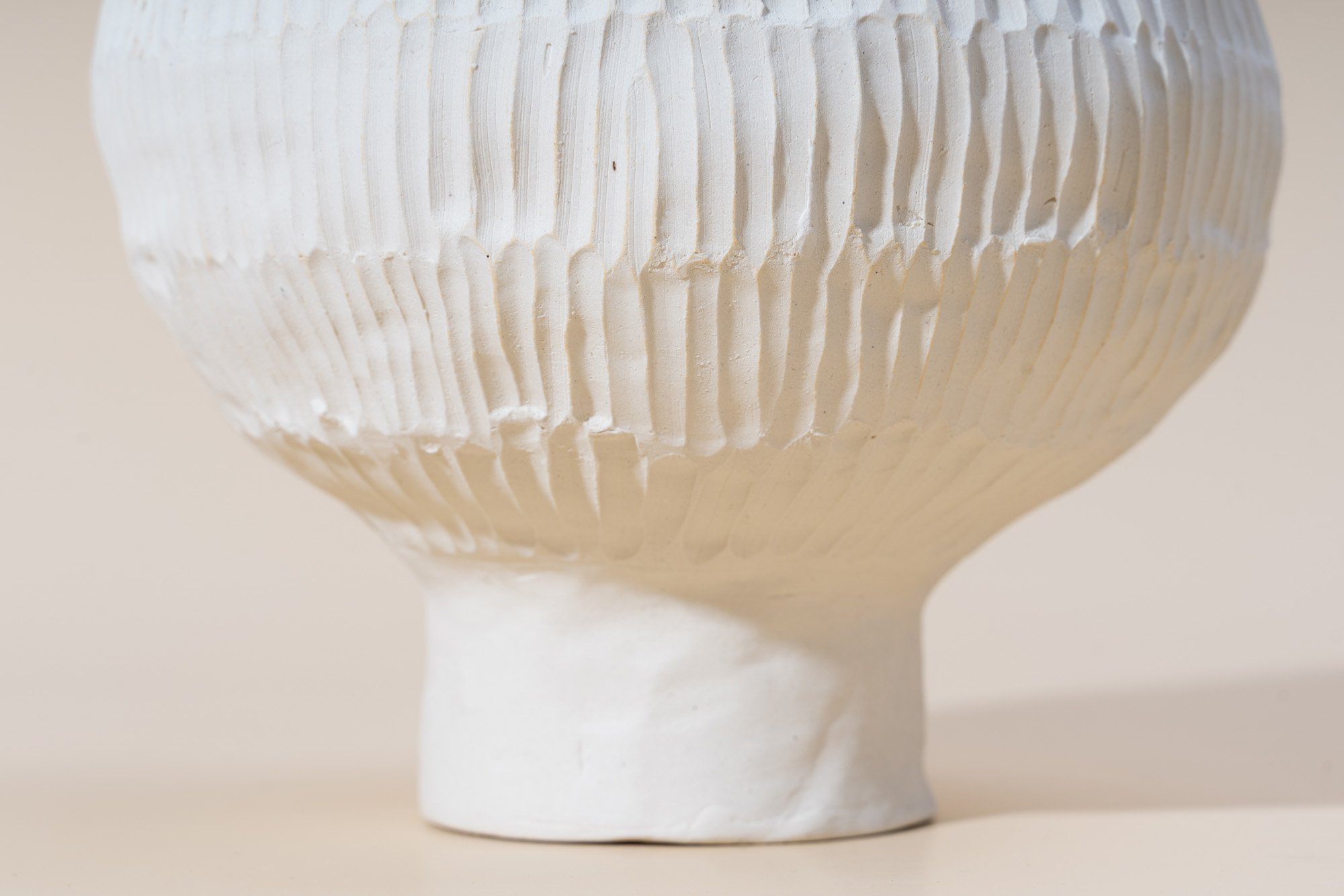Close-up of a white ceramic vase with vertical ridges and an irregular, textured surface.