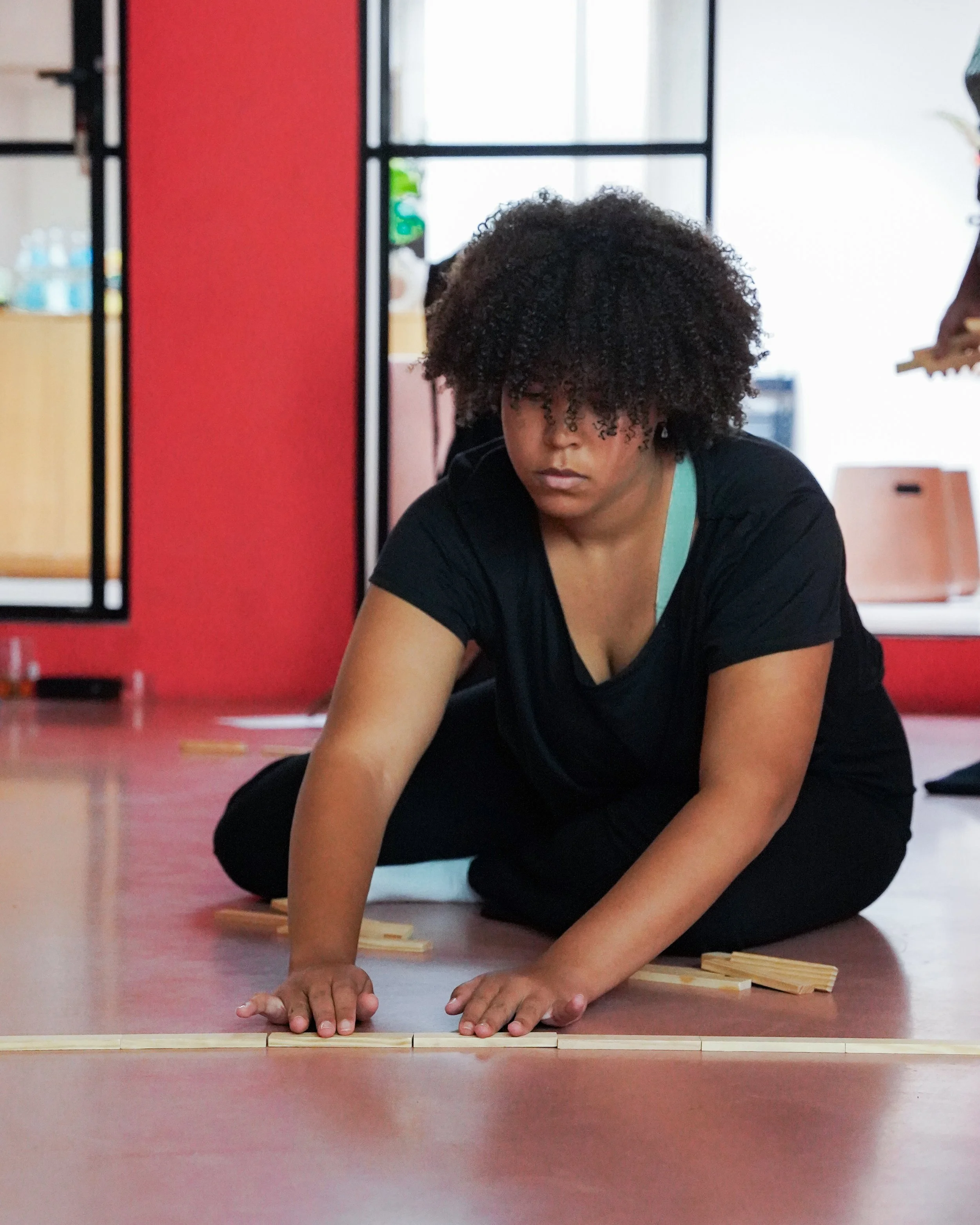 Woman kneeling on the floor arranging wooden tiles or pieces.