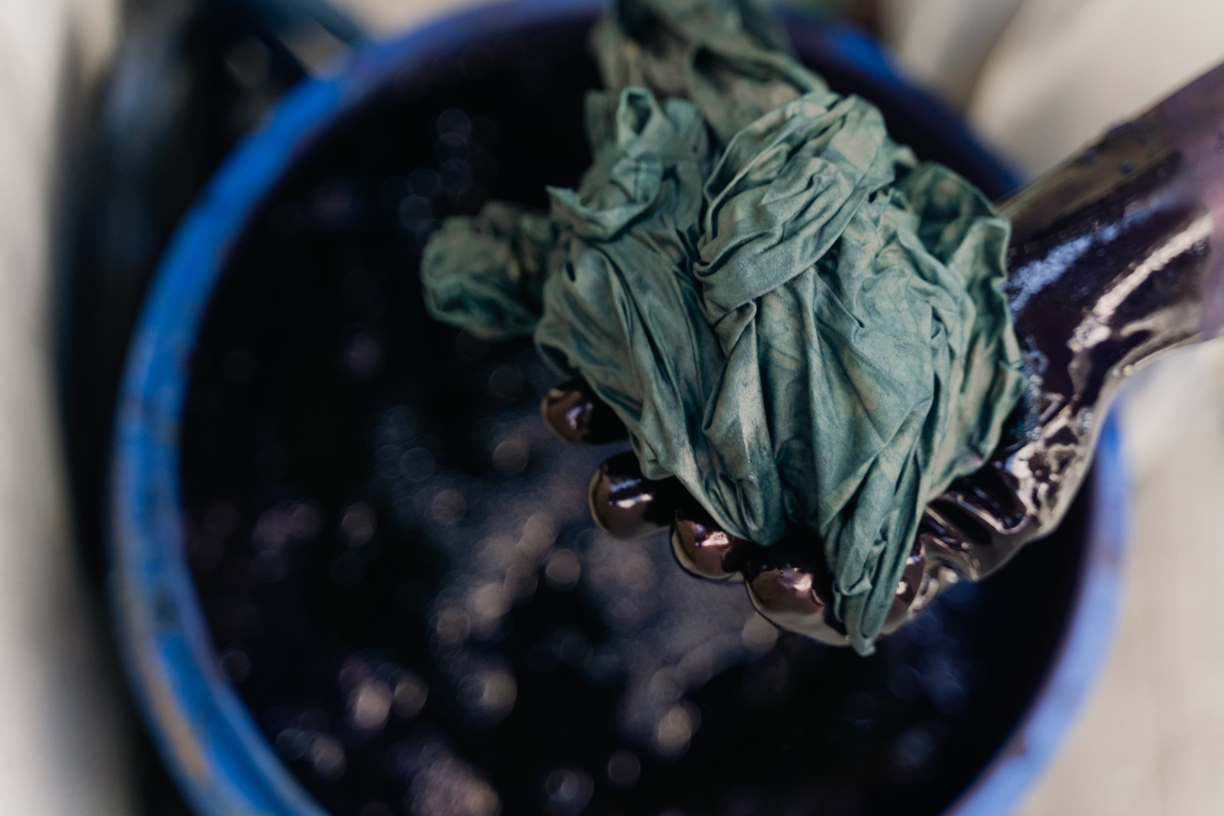 A paintbrush with dried green paint and a crumpled green cloth resting in a dark paint bucket.