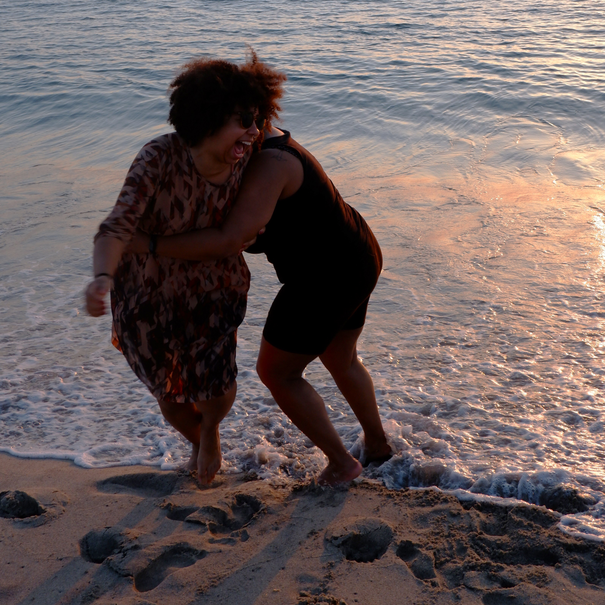 Two women laughing and playing in the surf at the beach during sunset.