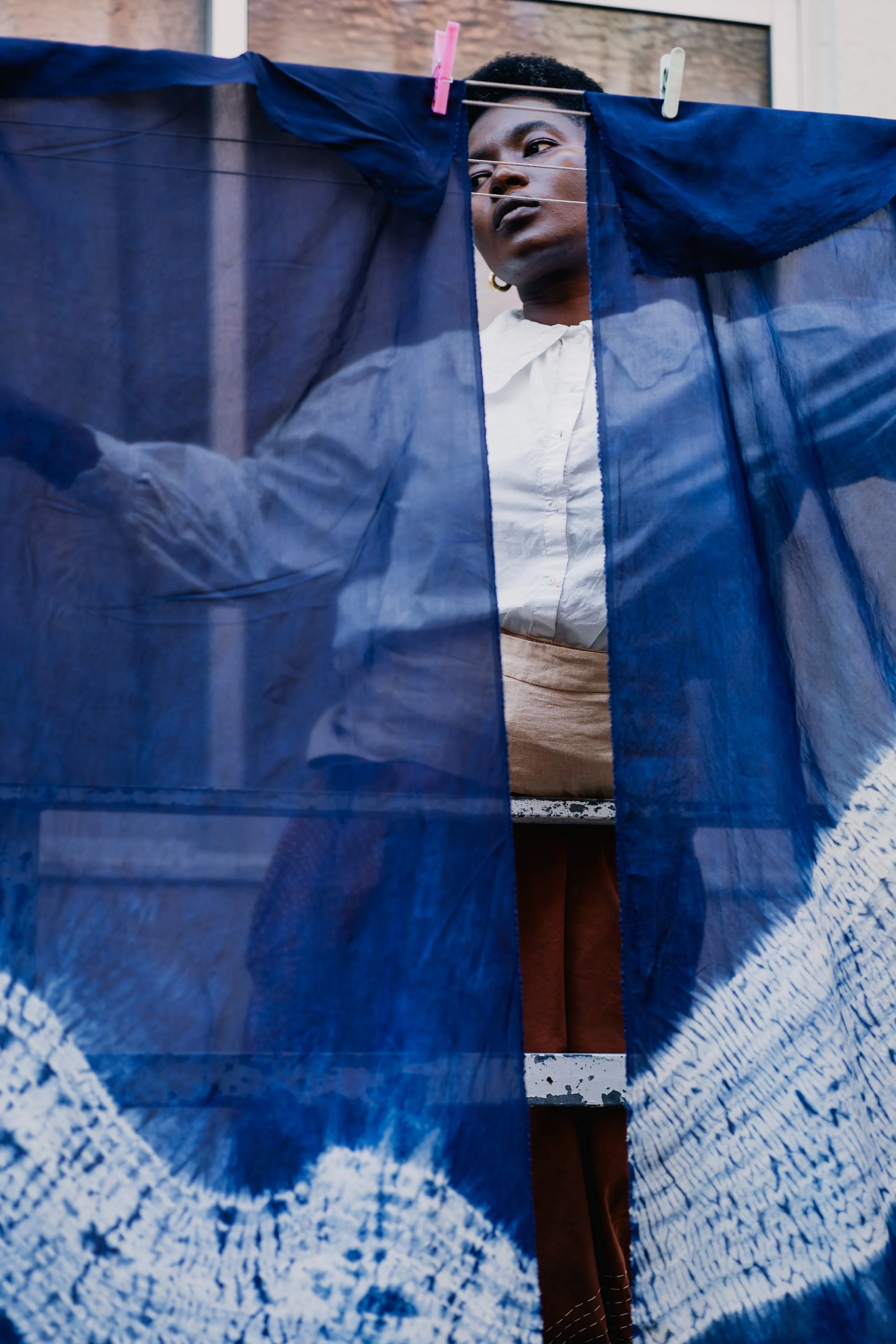 A woman hanging blue and white patterned fabric on a clothesline outdoors.
