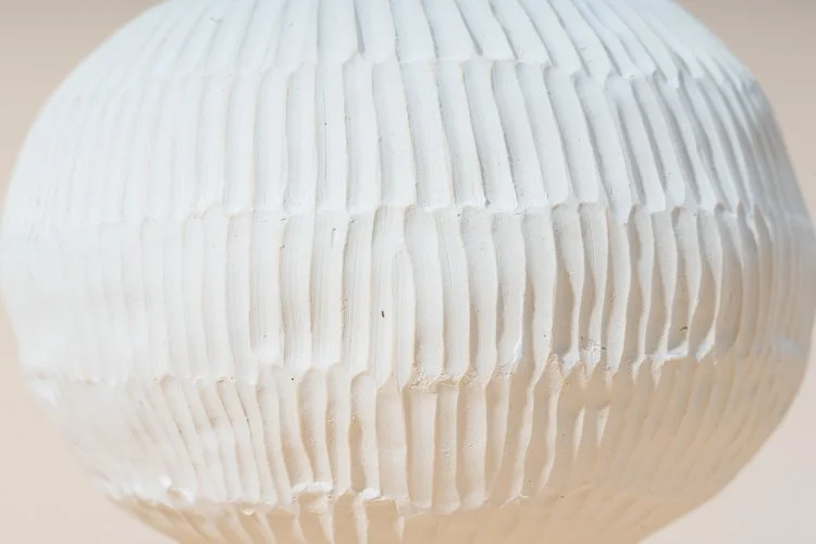 Close-up of a round white ceramic or plaster object with vertical ridges.