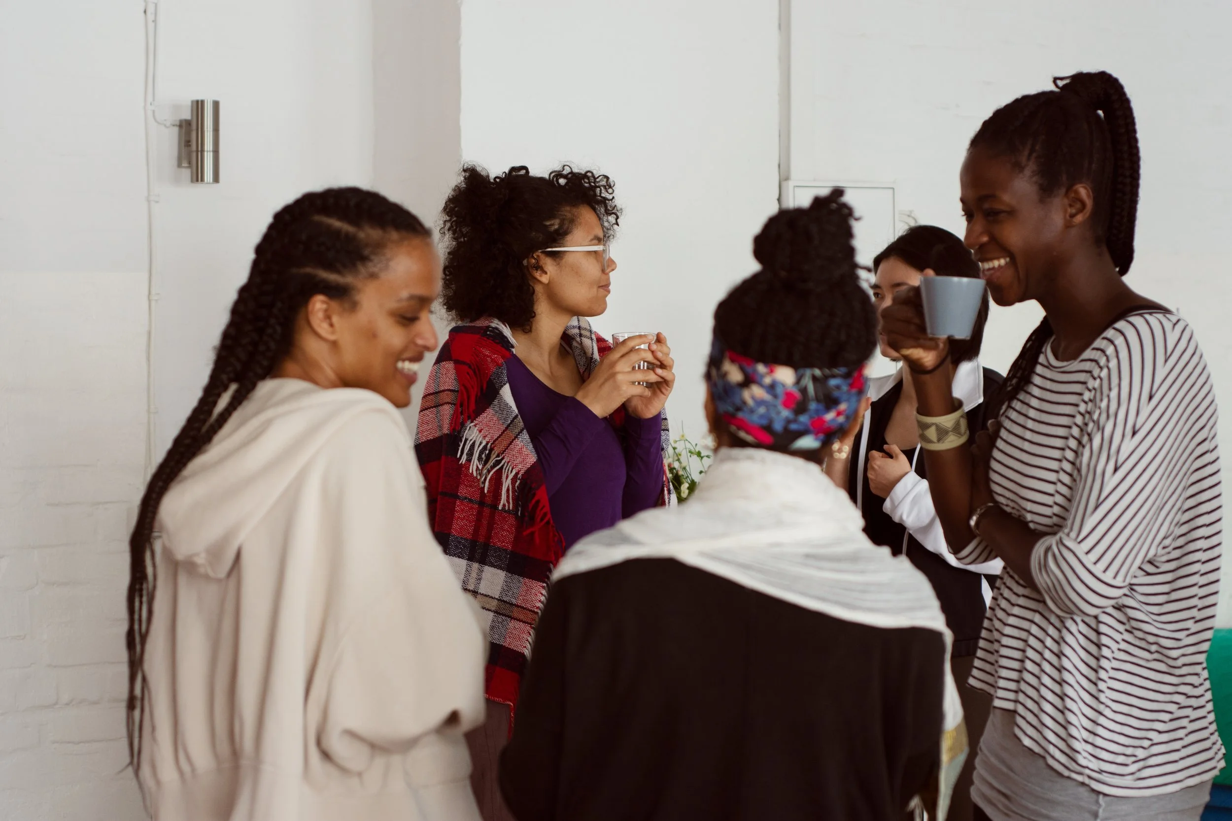 Group of diverse women chatting and smiling indoors, one holding a mug.