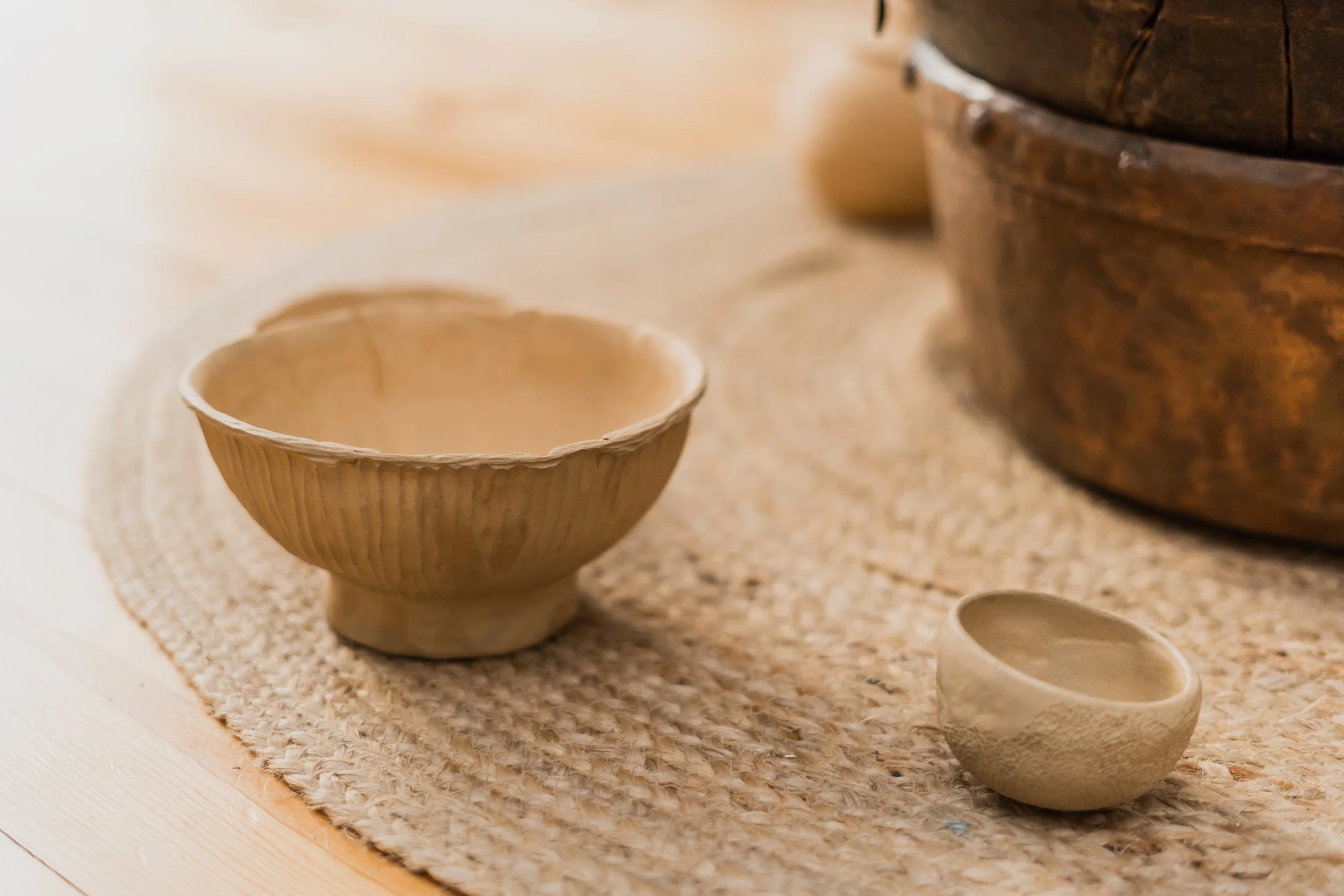 Two ceramic bowls on a woven rug, with a large wooden bowl in the background.