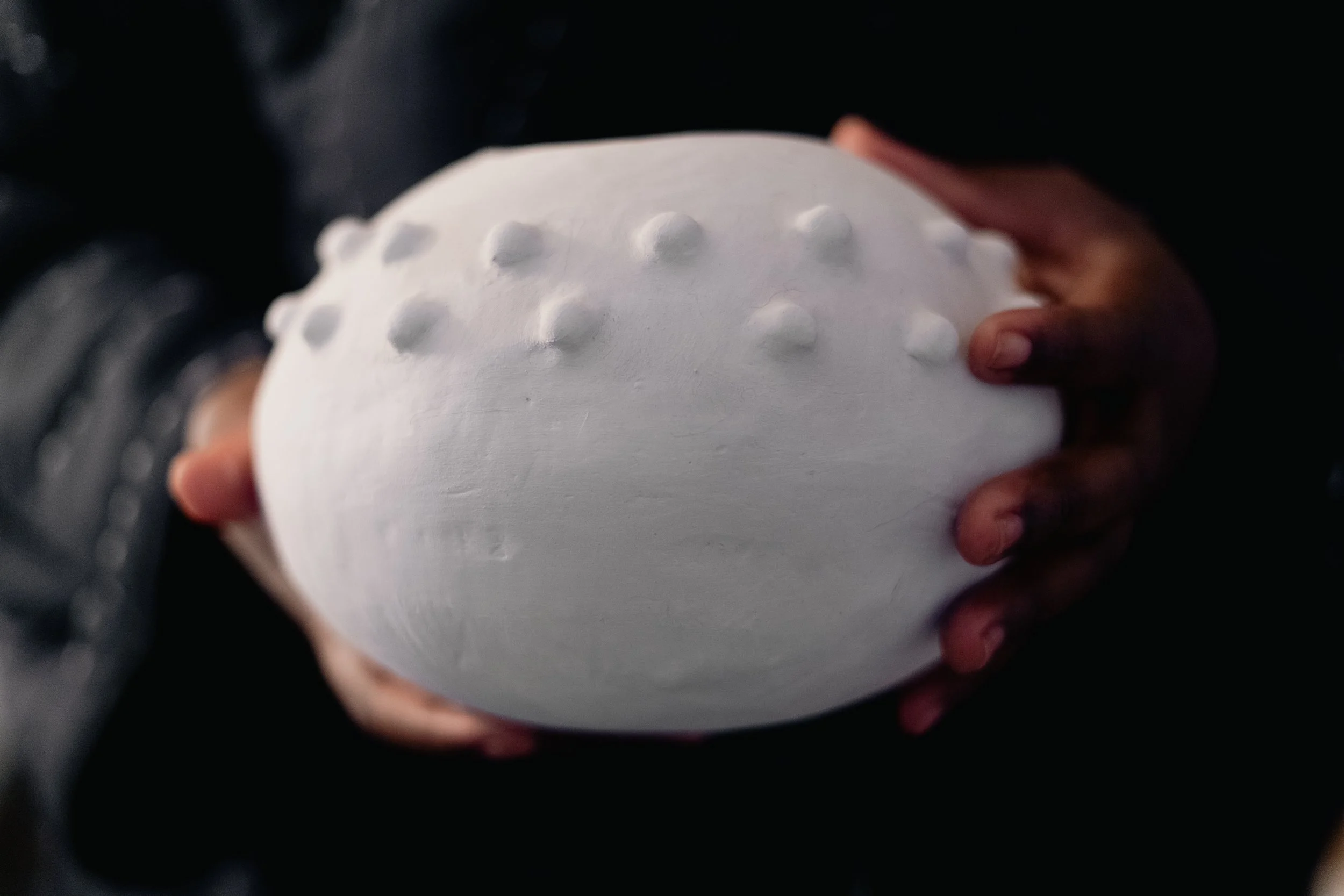 Person holding a white ceramic object with raised dots on its surface.