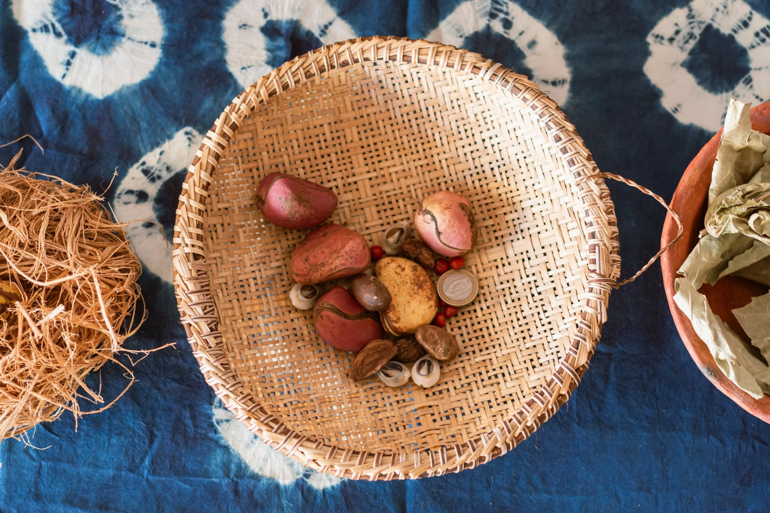 Wicker basket containing assorted stones, seeds, and small decorations on a blue and white patterned fabric.