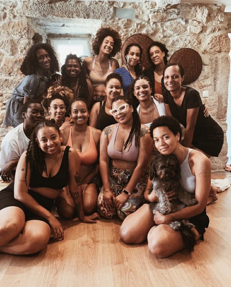 Group of 13 women and one dog sitting and standing together in a cozy room with stone walls, smiling at the camera.